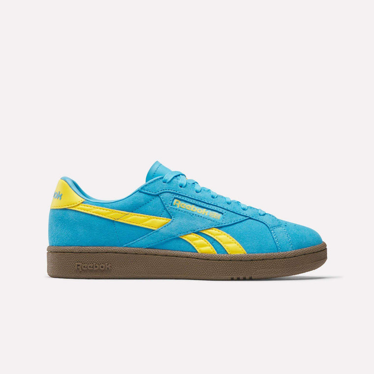 The Reebok Club C Grounds UK Shoes feature a blue suede upper with yellow accents and branding, brown rubber sole, and are pictured in side profile on a plain white background.