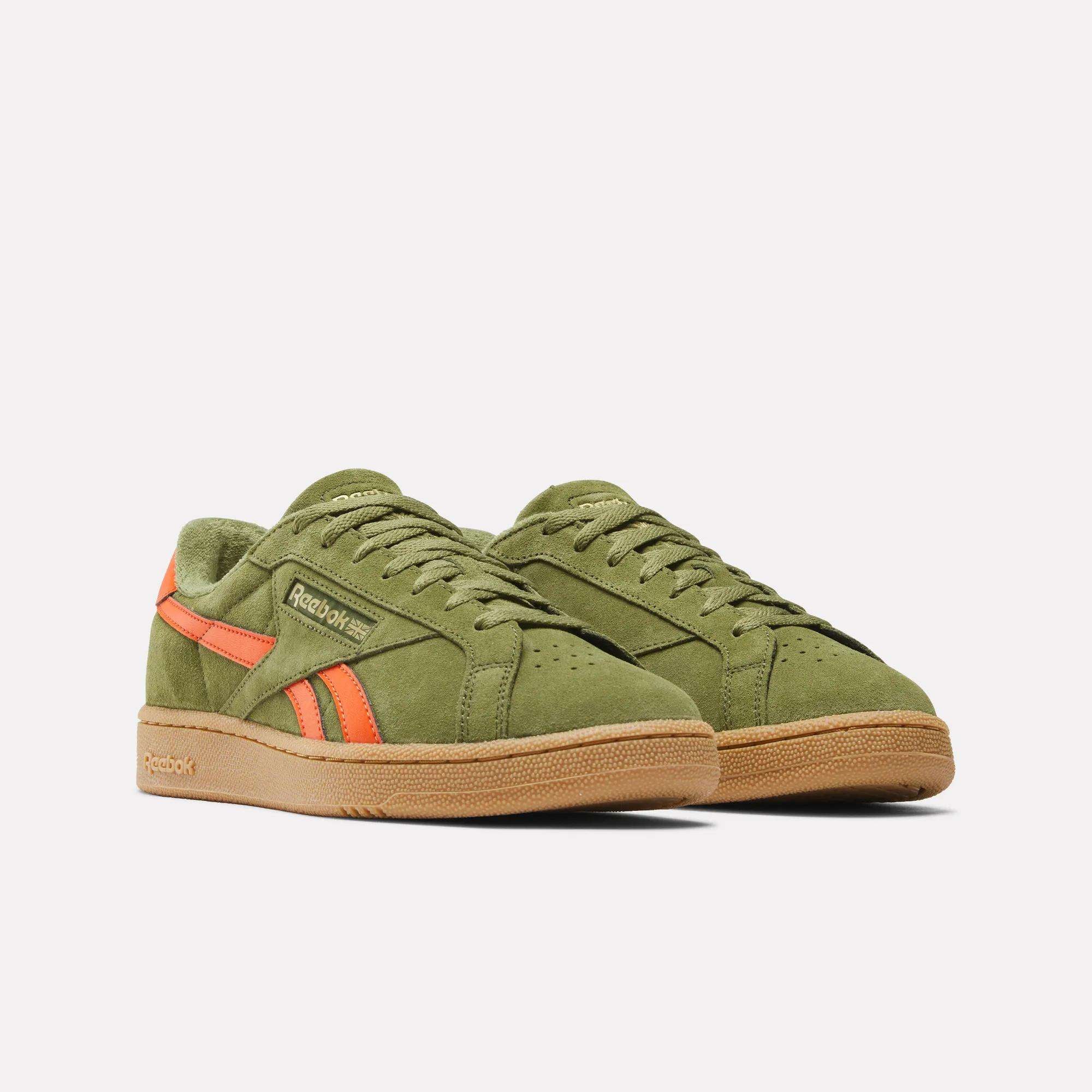 A pair of Reebok Club C Grounds UK Shoes in olive green suede with orange accents and gum rubber soles, highlighting classic Reebok heritage, displayed on a plain white background.