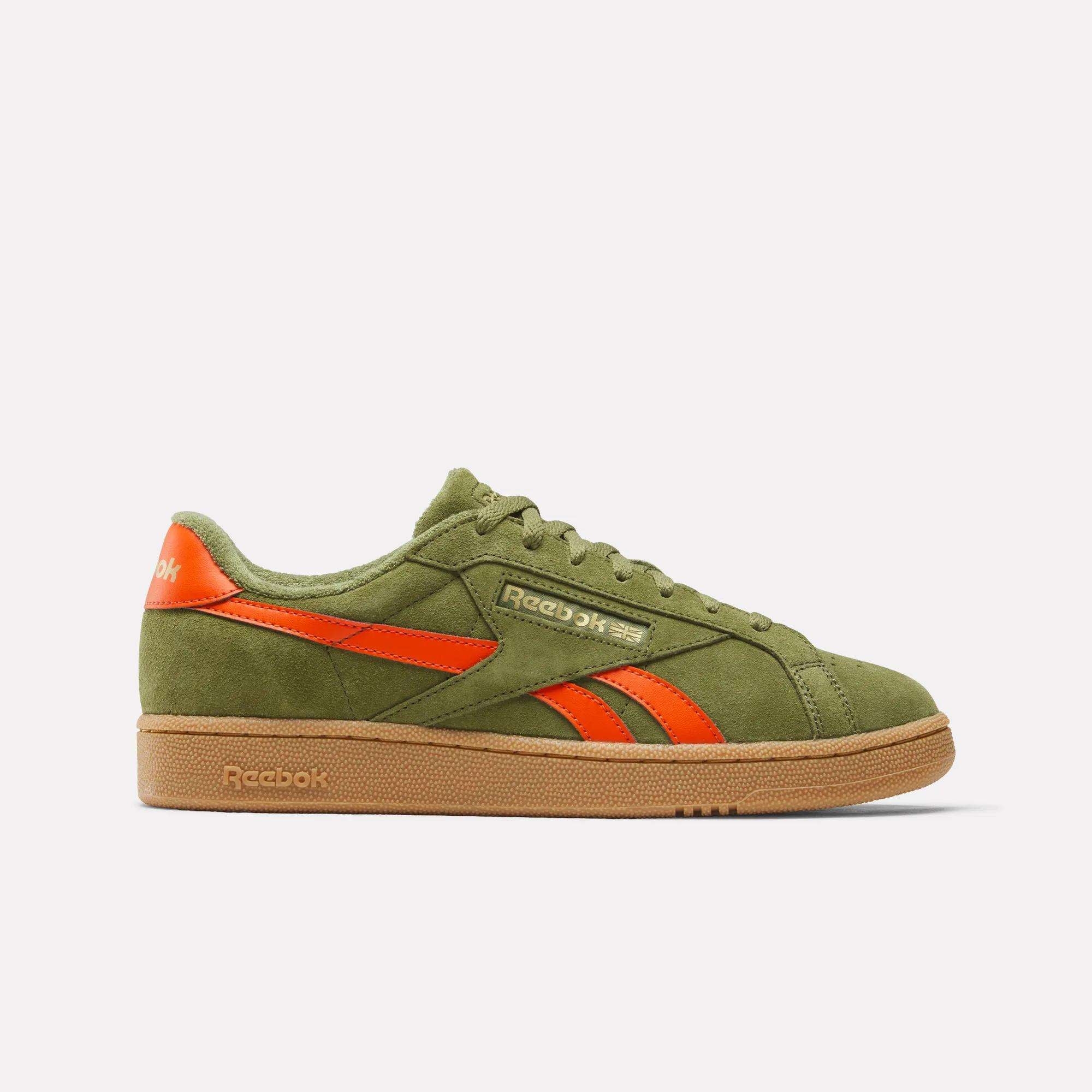 The Reebok Club C Grounds UK Shoes feature green suede with orange accents, including the logo and stripes, plus a light brown rubber sole—classic heritage style shown in side profile on a plain white background.