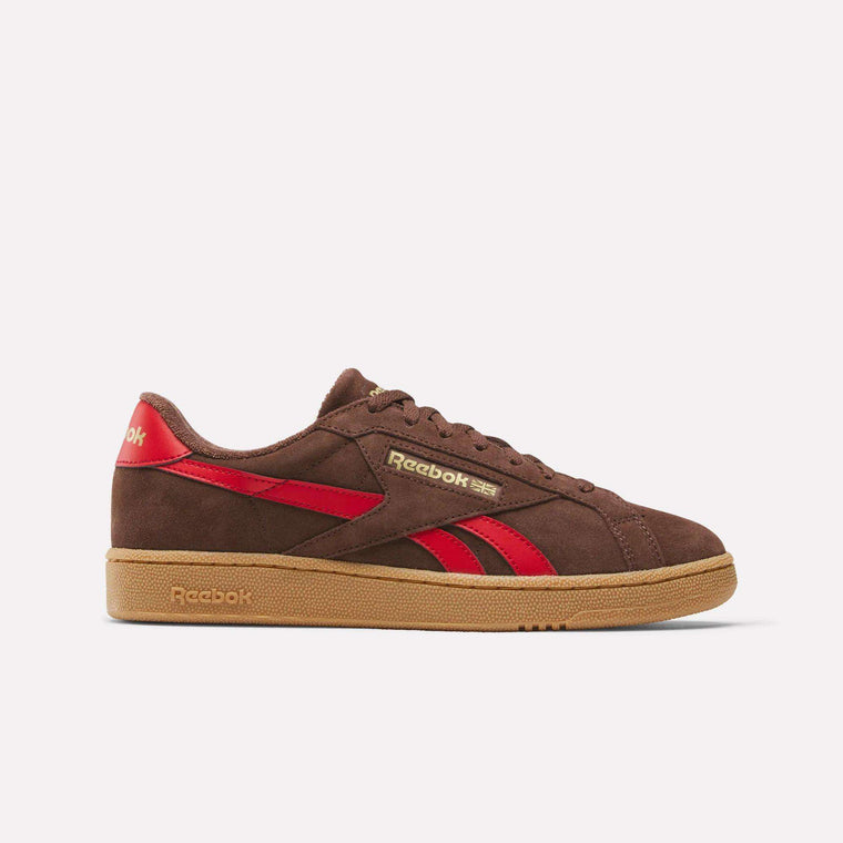 The Reebok Club C Grounds UK Shoes feature a brown suede upper with red accents, gold detailing, and a light brown rubber sole—classic archive-inspired style shown in side profile on a white background.