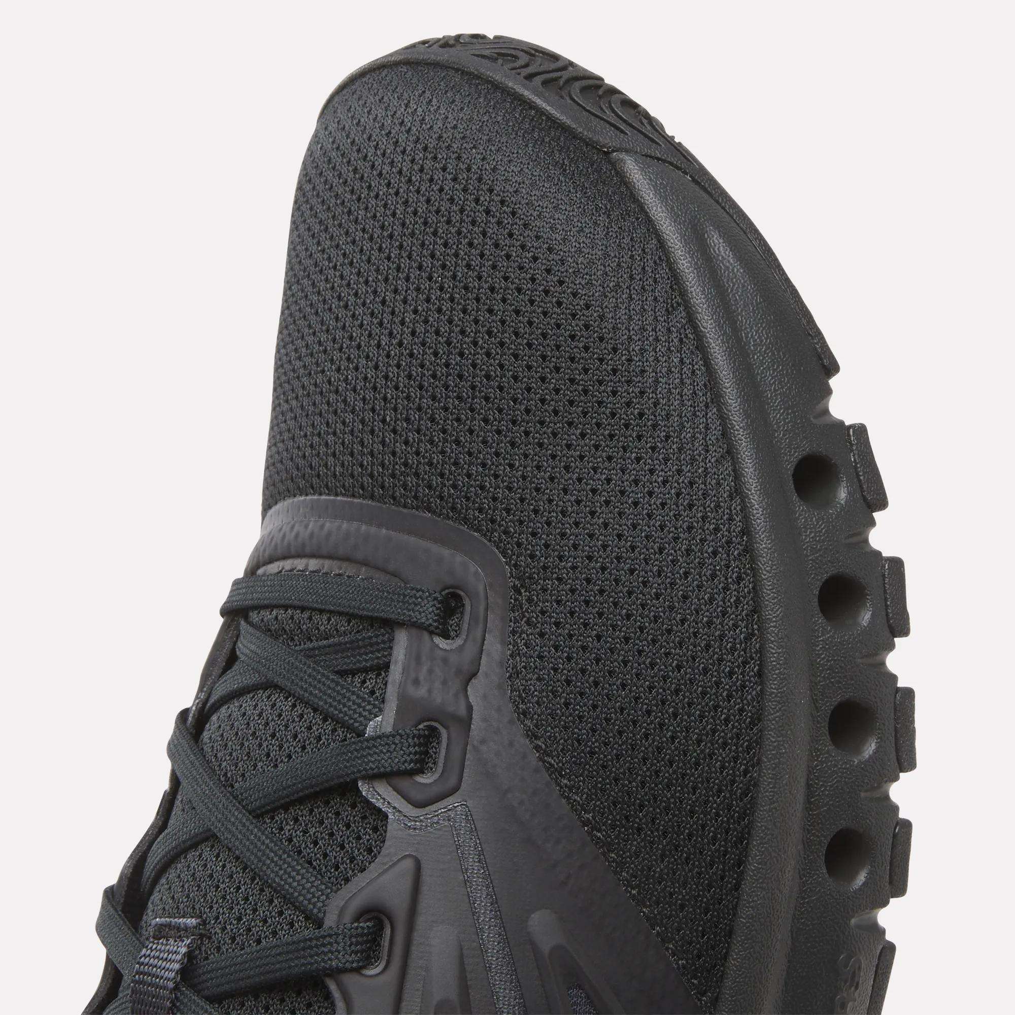 Close-up of the toe and side of Reebok Men's ERS Training Shoes, featuring a textured mesh upper, synthetic overlays, and a distinctive midsole with circular cutouts for premium cushioning.