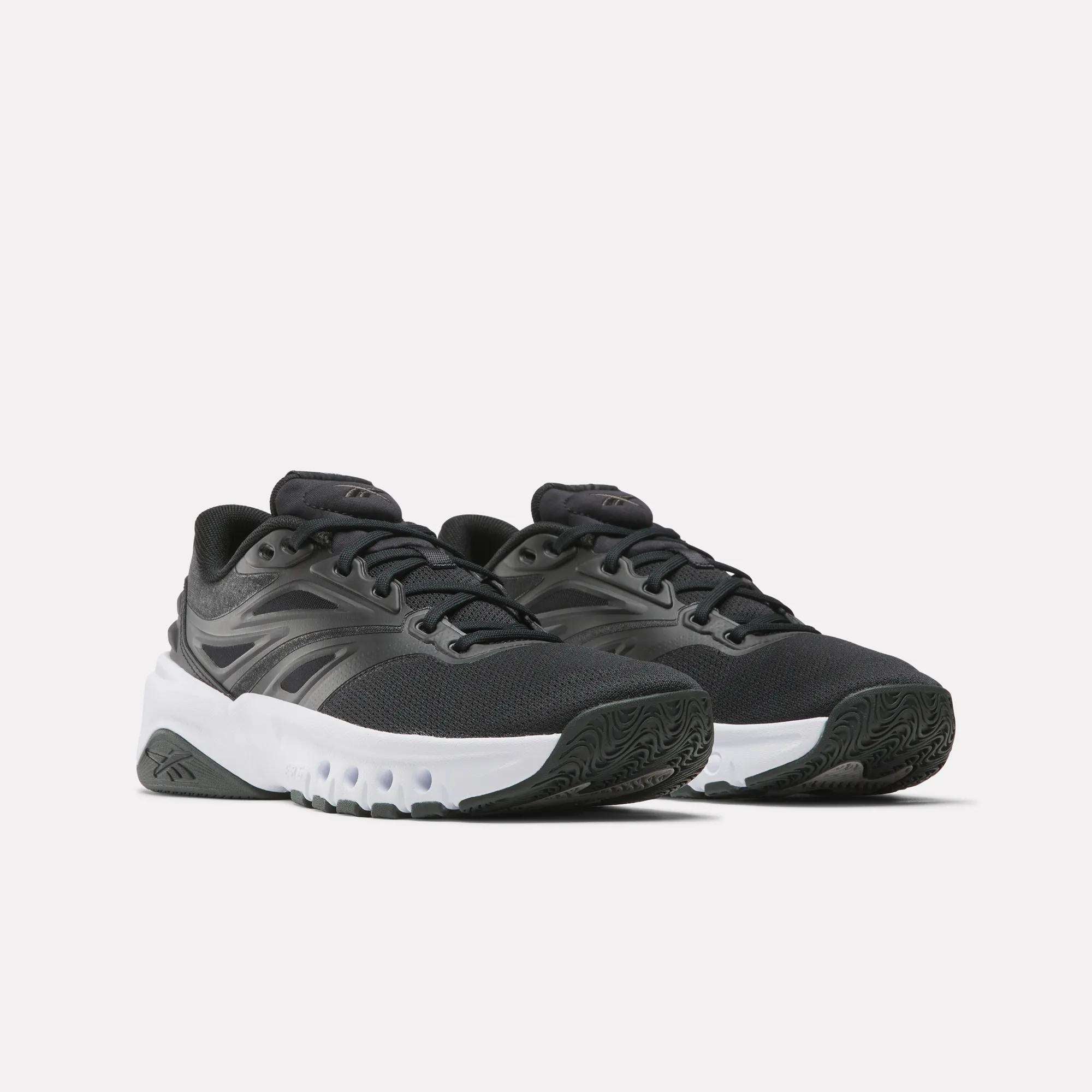 The Reebok Men's ERS Training Shoes feature a black design with white chunky soles, black laces, and a subtle side logo. These shoes provide premium cushioning and are shown on a plain light background.