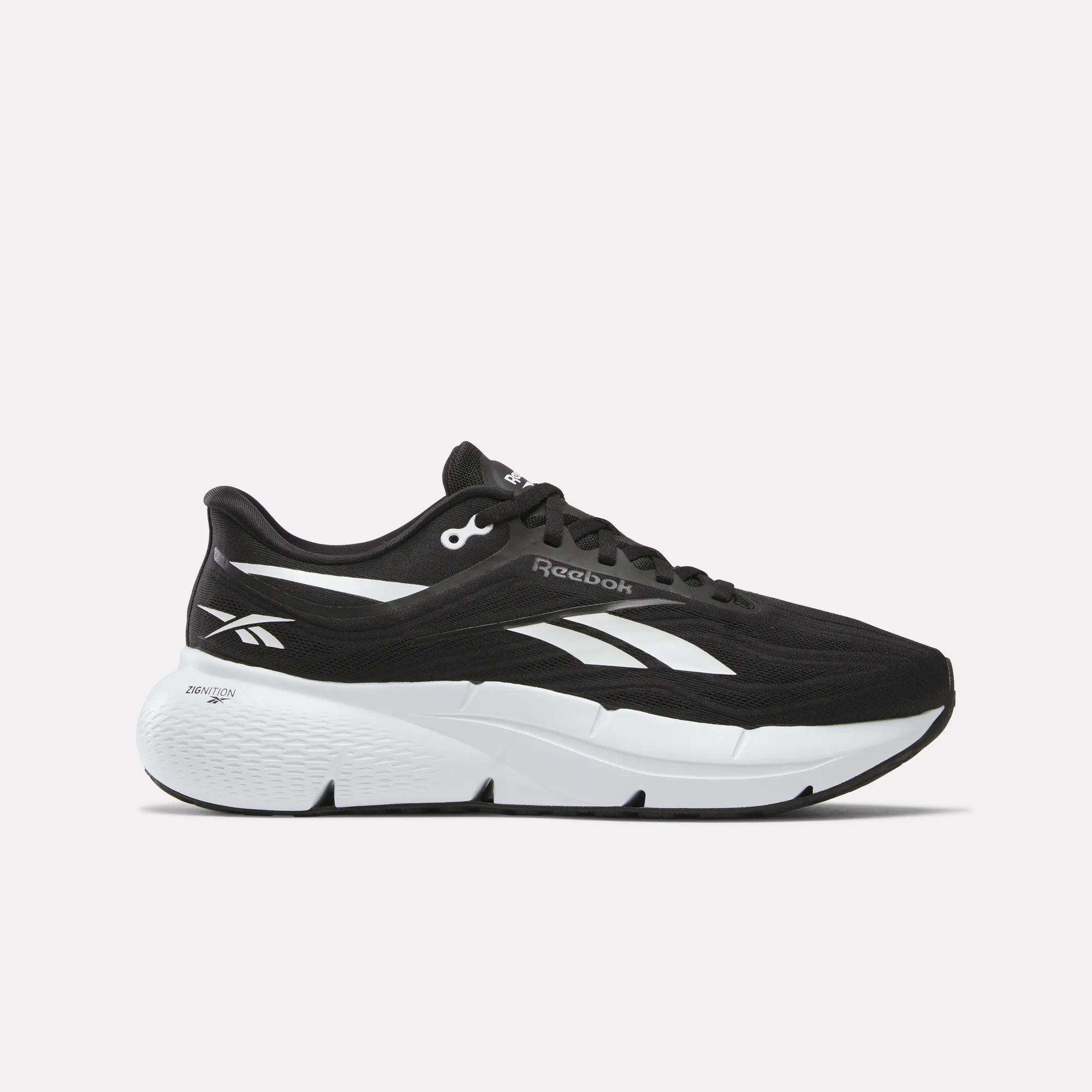 The Men's Zignition Running Shoes by Reebok feature a black design with white and silver accents, a thick cushioned white sole, and signature Reebok logos—ideal for new runners who value style and comfort.