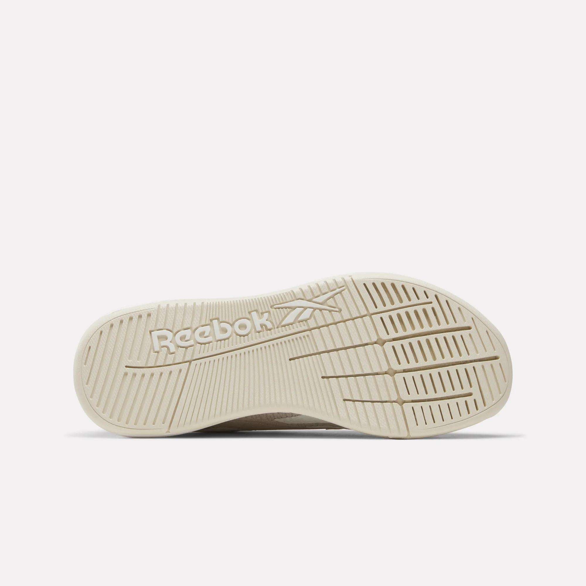 The image displays the outsole of the Women’s Nano X5 Training Shoes by Reebok, showcasing the logo and diagonal grooves for traction. The sole is viewed from below against a white background, highlighting this beige women’s training shoe.