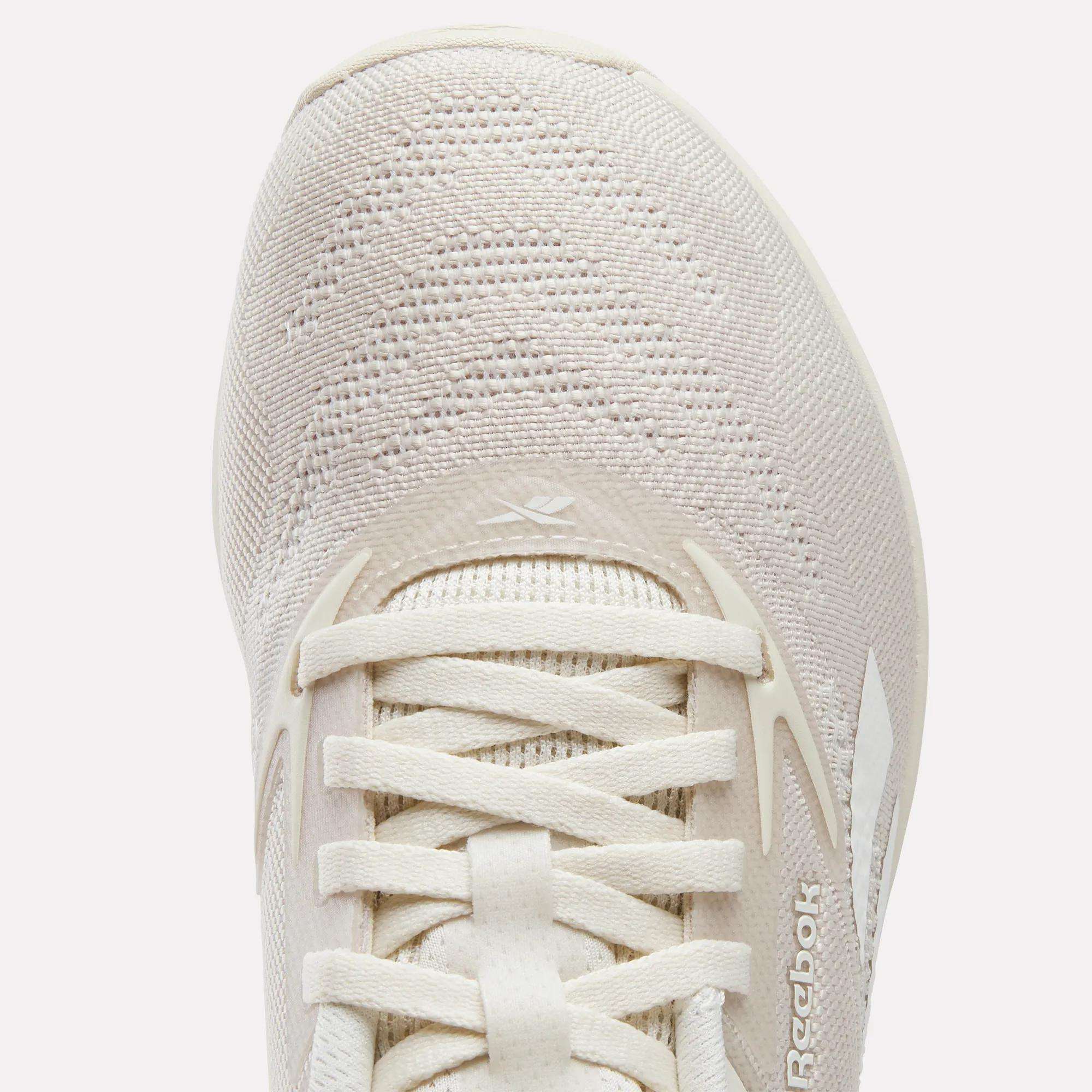 Close-up of the upper part of the Women's Nano X5 Training Shoes by Reebok in light beige, highlighting the knit fabric, laces, and side Reebok logo—ideal for women seeking both style and performance.