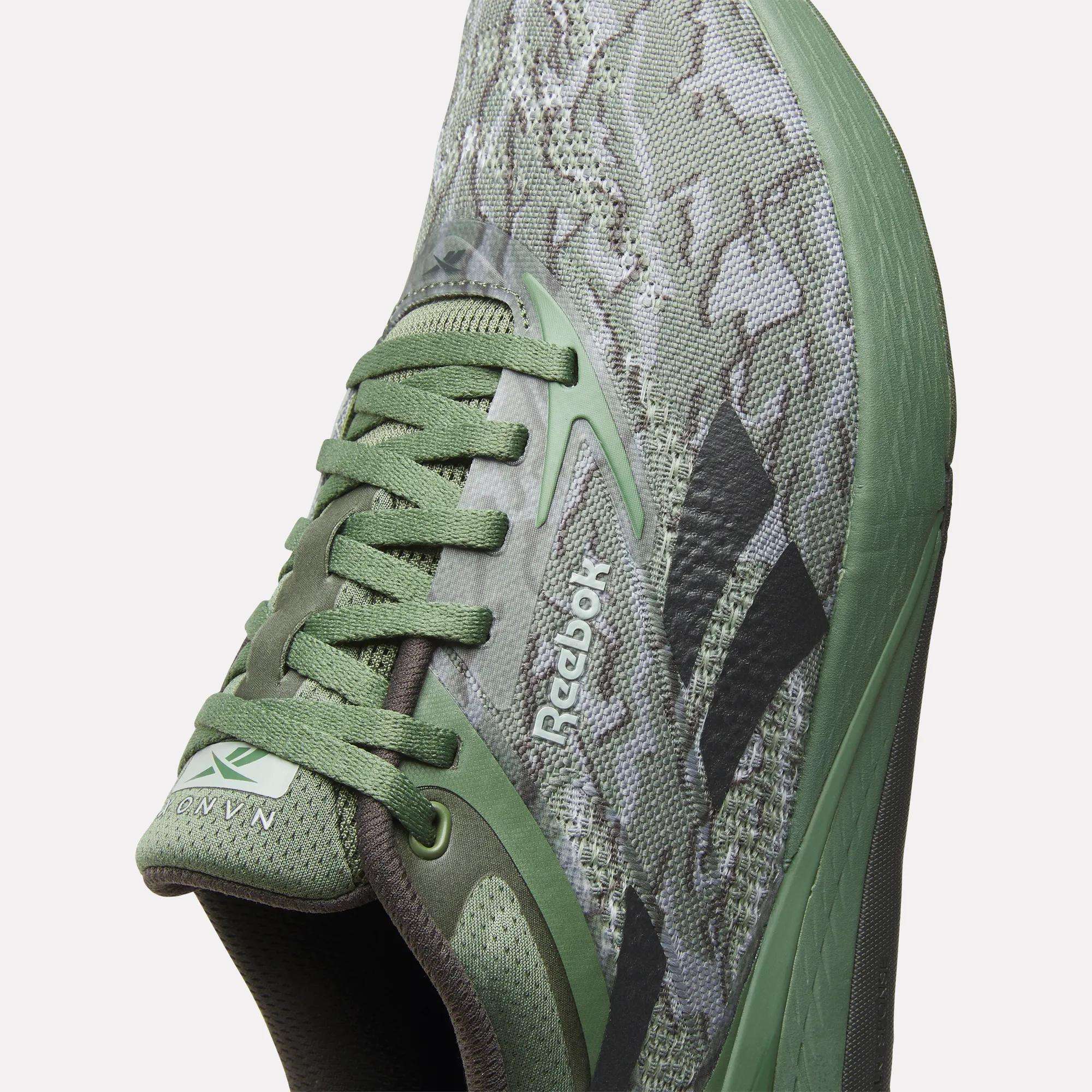 Close-up view of Reebok Nano X5 Training Shoes for men, featuring a green camouflage pattern, green laces, black Reebok logo, breathable mesh upper, and textured sole for comfort.