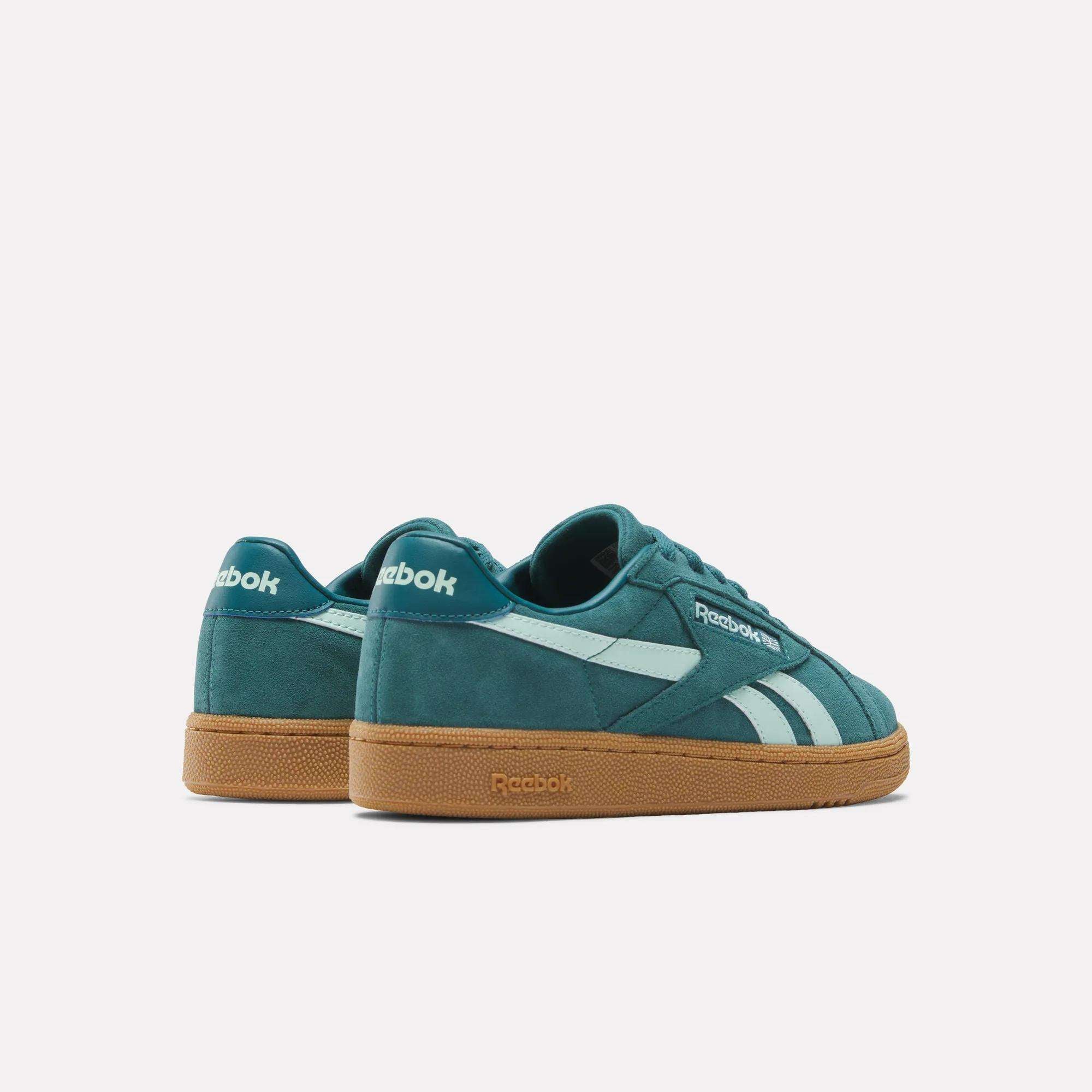 The Women's Club C Grounds UK Shoes by Reebok feature a teal suede upper, white side stripes, and gum rubber soles. Displayed on a plain white background, one shoe is set slightly behind the other for a stylish look.