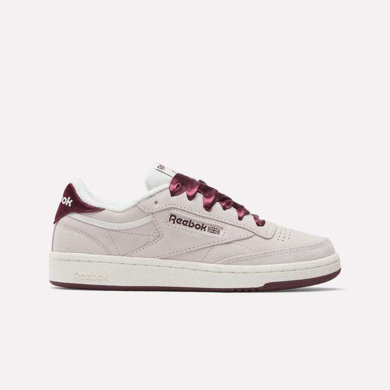 The Reebok Women's Club C 85 Shoes feature a light pink upper with maroon accents and laces, plus a white sole, displayed in side profile against a plain white background.