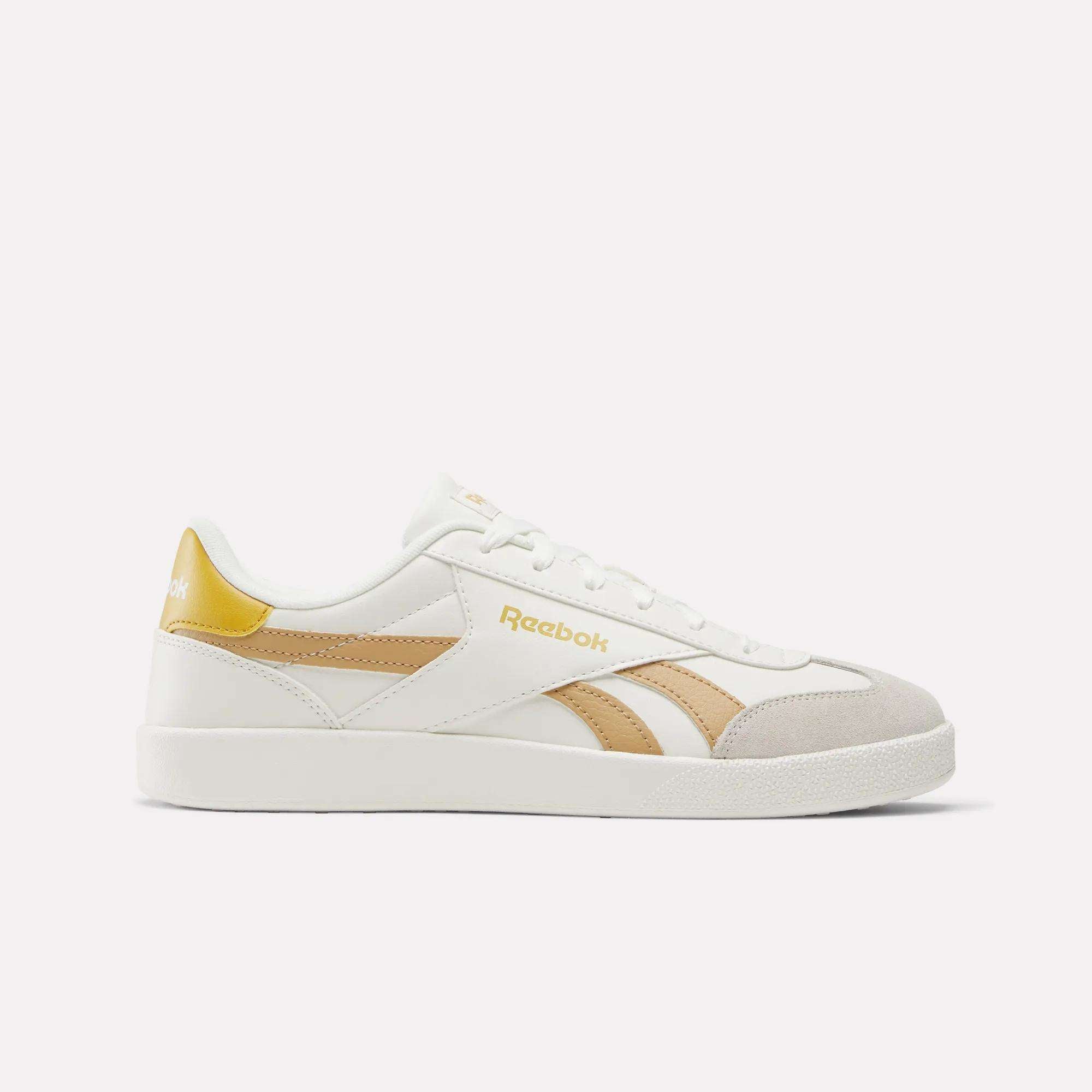 The Reebok Smash Edge Shoes feature a white design with beige and gold accents and the Reebok logo on the side and heel—ideal for fans of classic indoor soccer style, shown against a plain white background.