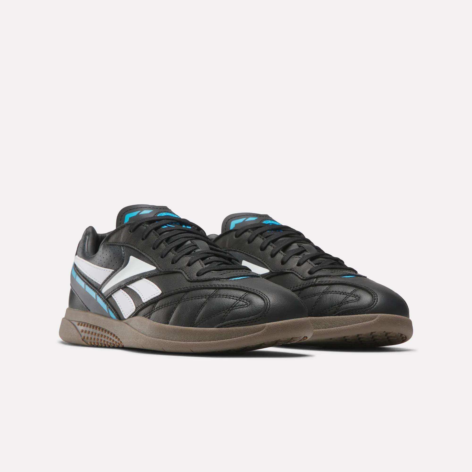 Reebok Hammer Street Shoes are black athletic sneakers in full-grain leather with white and light blue accents, brown rubber soles, a white side logo, and soccer-inspired design, displayed on a plain white background.
