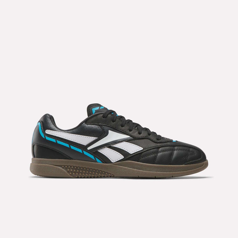 The Reebok Hammer Street Shoes feature a black, indoor-soccer-inspired design with full-grain leather, blue and white accents, gum rubber sole, black laces, and a white side logo—shown on a plain white background.