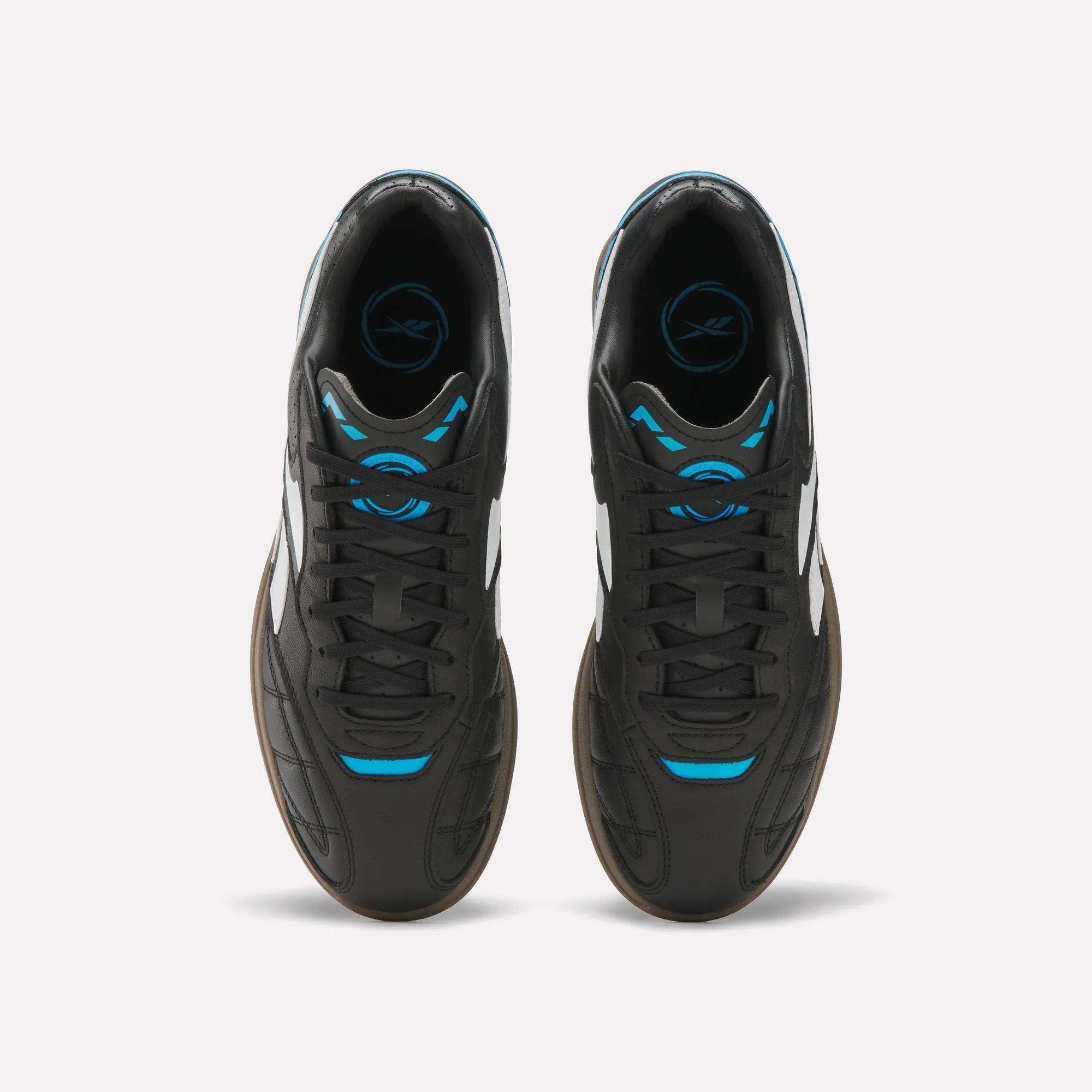 Top view of Reebok Hammer Street Shoes—black full-grain leather with white side stripes, blue accents at the laces and tongue, and gum outsoles—soccer-inspired and set side by side on a white background.