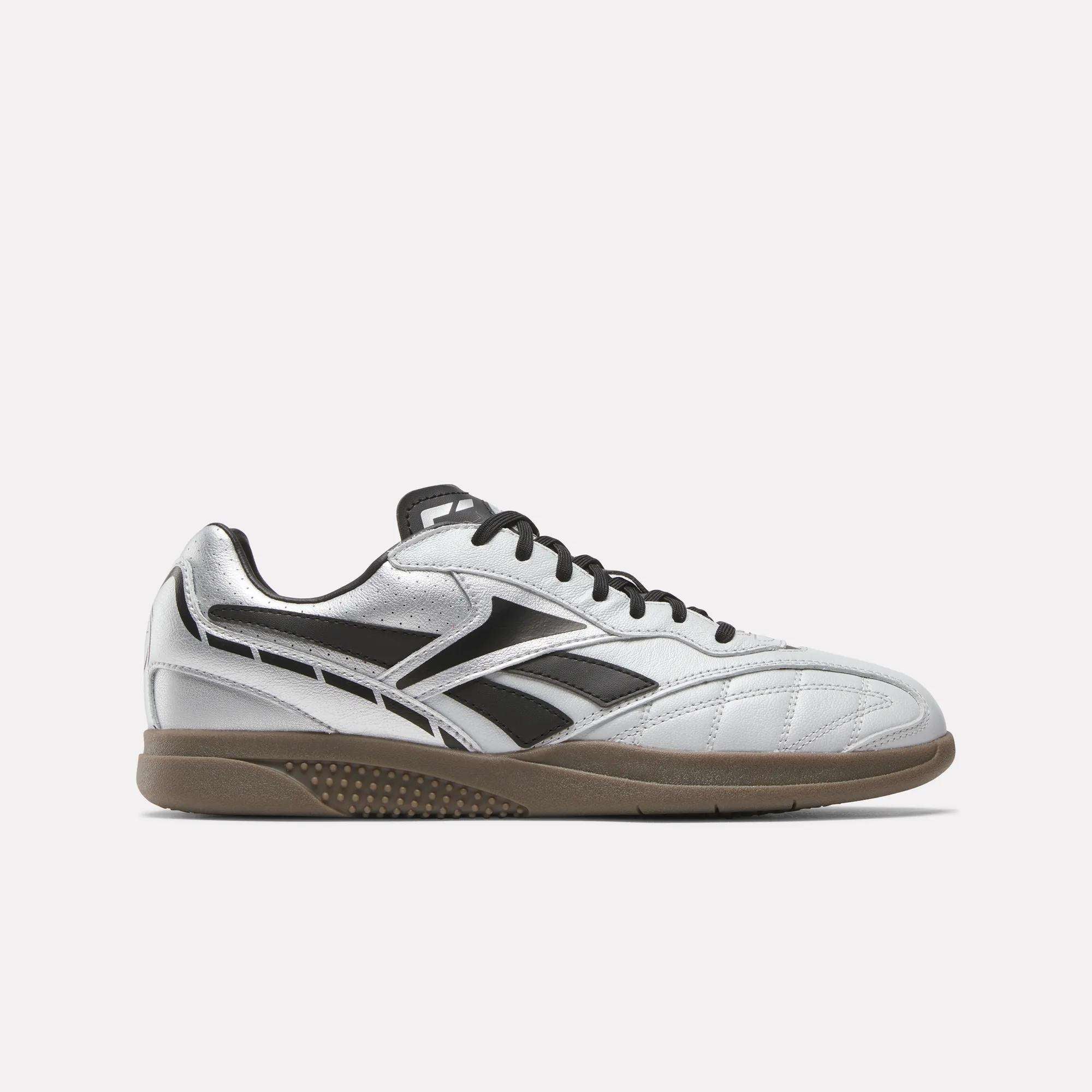 The Reebok Hammer Street Shoes are silver and black low-top sneakers made from full-grain leather, featuring black laces, side logo details, and a brown rubber sole, displayed against a plain white background.