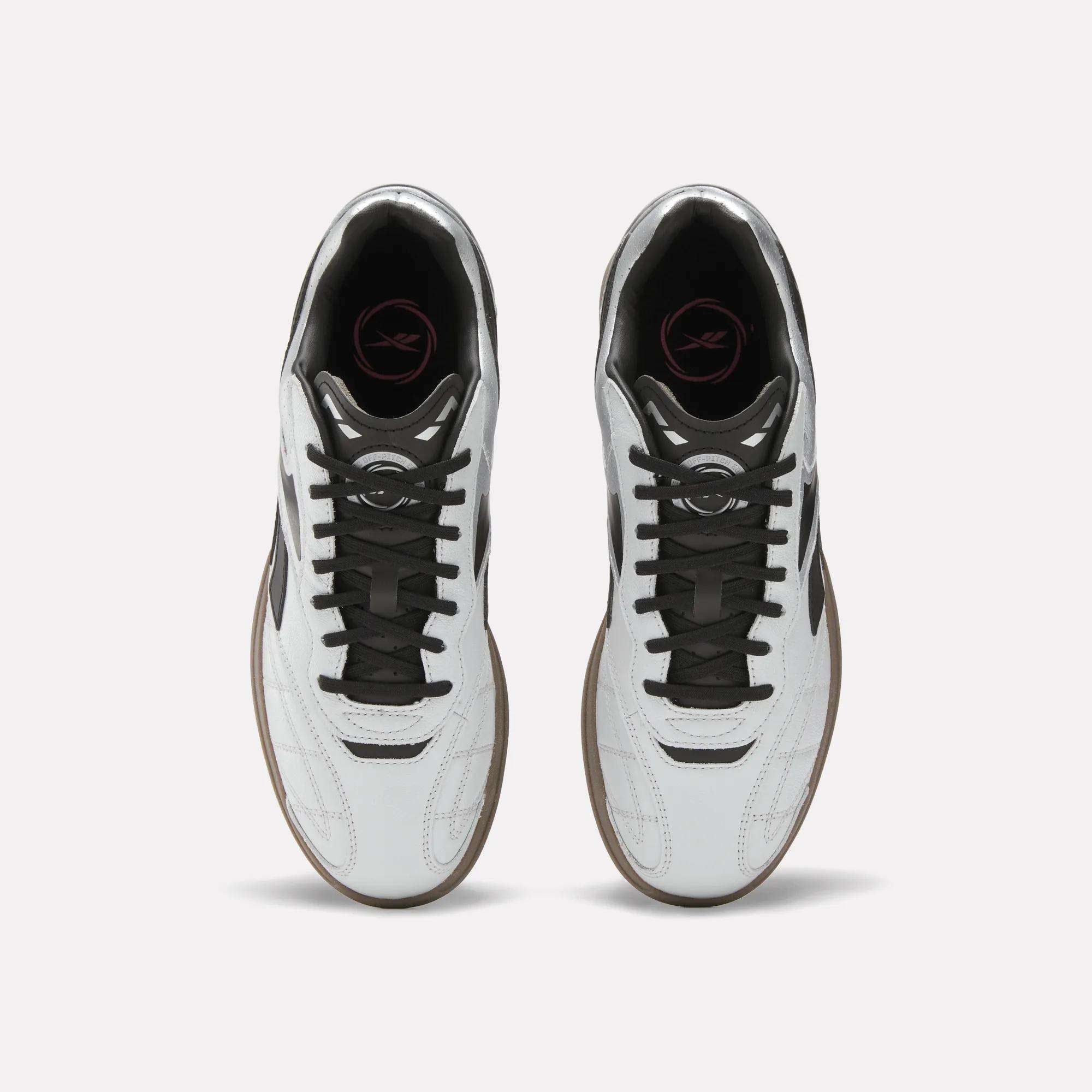 Top view of Reebok Hammer Street Shoes—soccer-inspired full-grain leather shoes with black laces, brown soles, and a pink logo on the black insole—placed side by side on a light background.