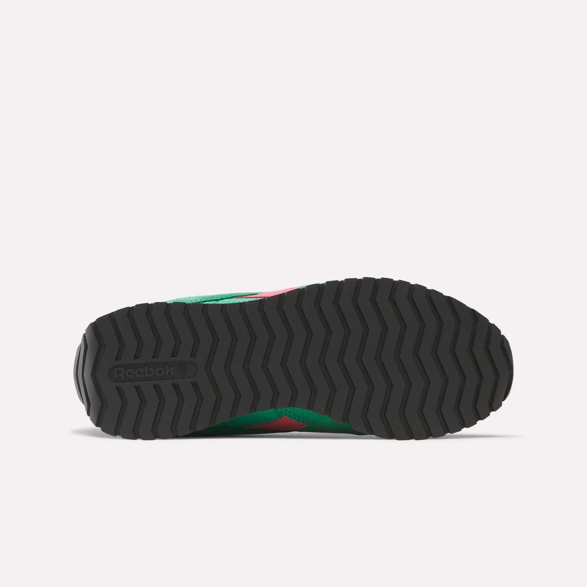 Bottom view of Reebok Women's Classic AZ Shoes featuring a black rubber outsole with a zigzag tread and Reebok logo. The green and pink midsole and upper of this retro running shoe are partially visible.