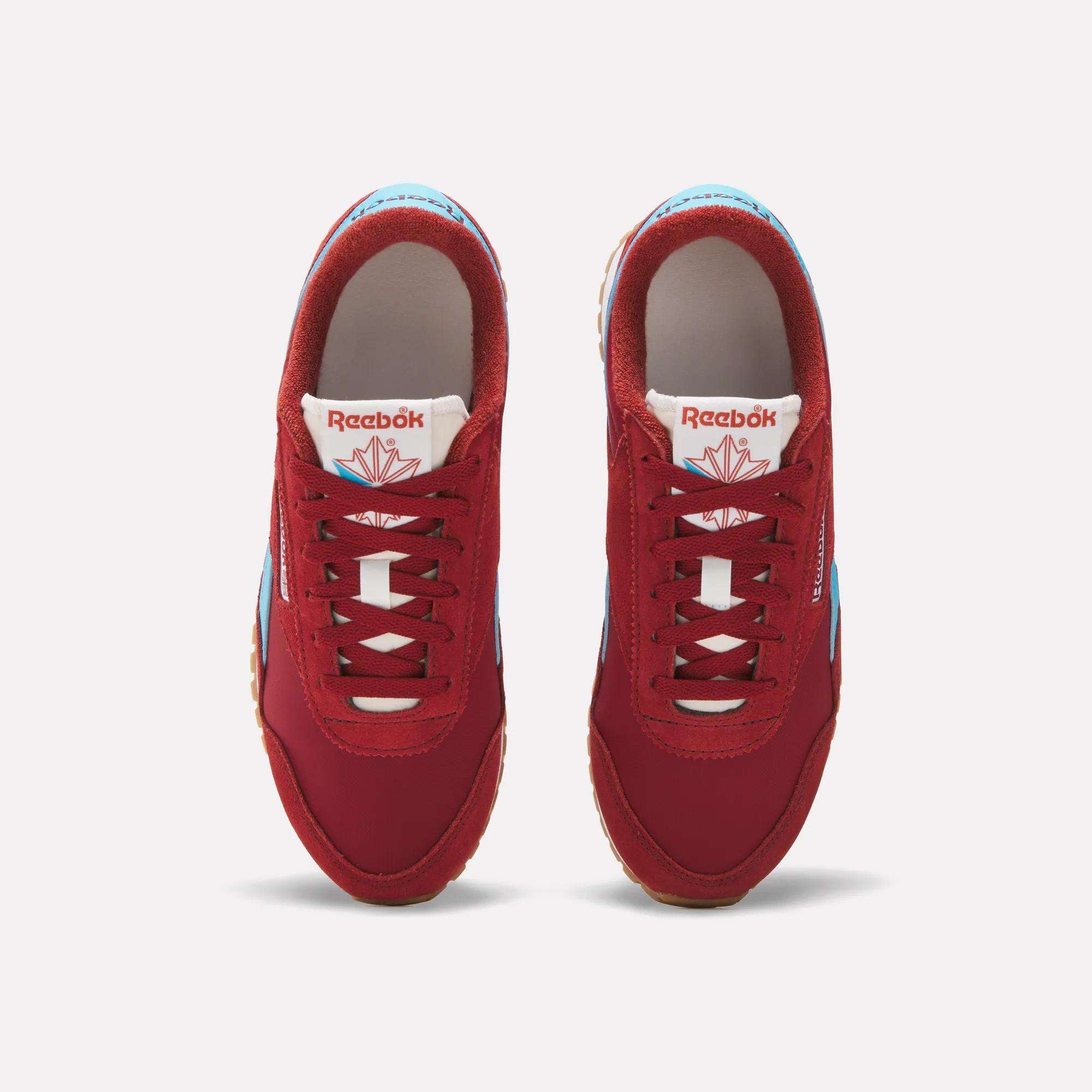 Top view of Reebok Women's Classic AZ Shoes in red with white laces, blue accents, and brown soles, side by side on a white background. The Reebok logo appears on the tongue, emphasizing their classic running-inspired style.