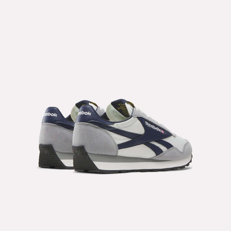 A pair of Reebok Aztec II Shoes in white, navy blue, and gray, shown from an angle highlighting the sides and heels, channels '80s marathon style with visible Reebok logos on the tongues and heels.