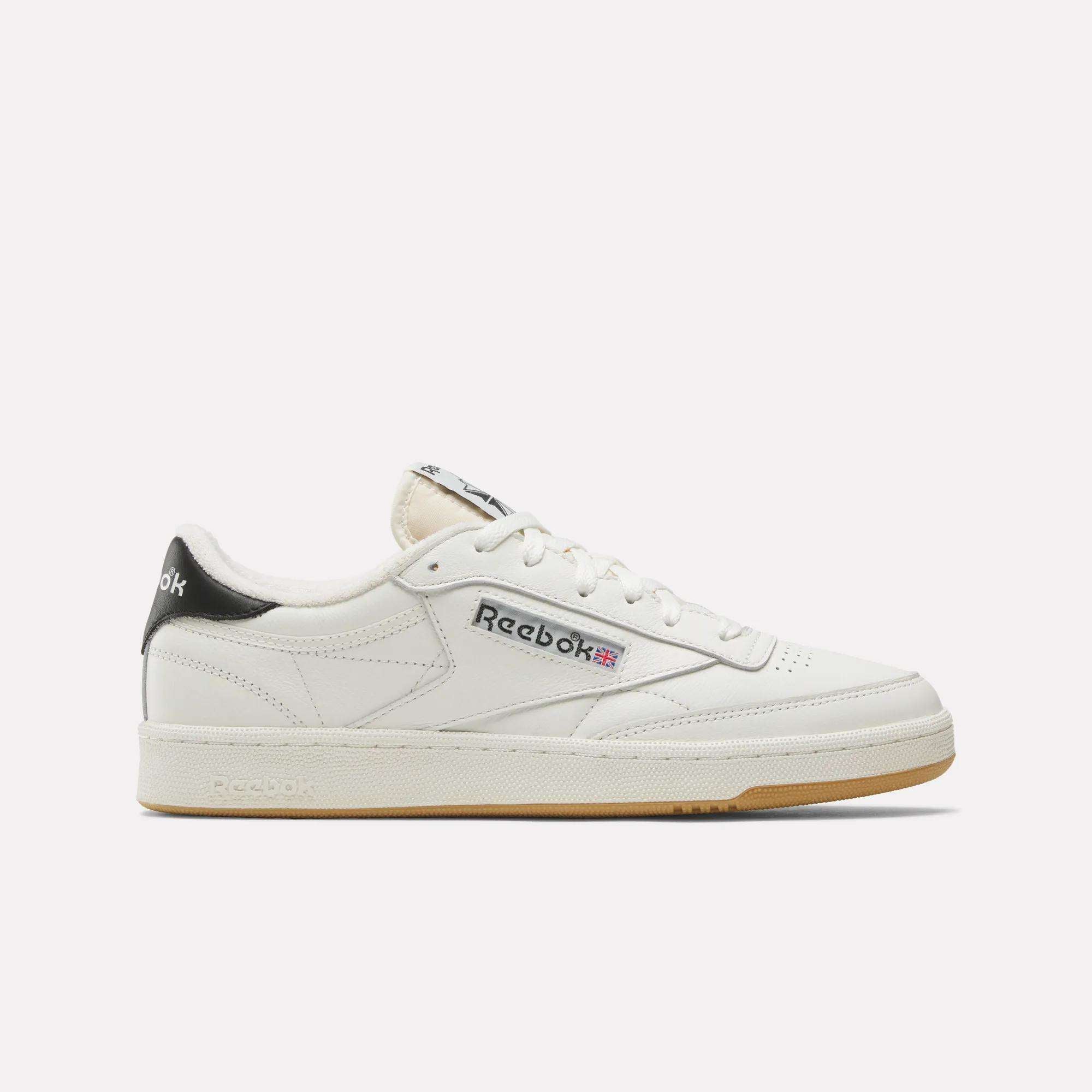 The Reebok Club C 85 Vintage Shoes feature a white leather upper, black heel tab, cream sole, and Reebok branding in black and red on the side. Shown on a white background, they deliver lightweight cushioning for all-day comfort.