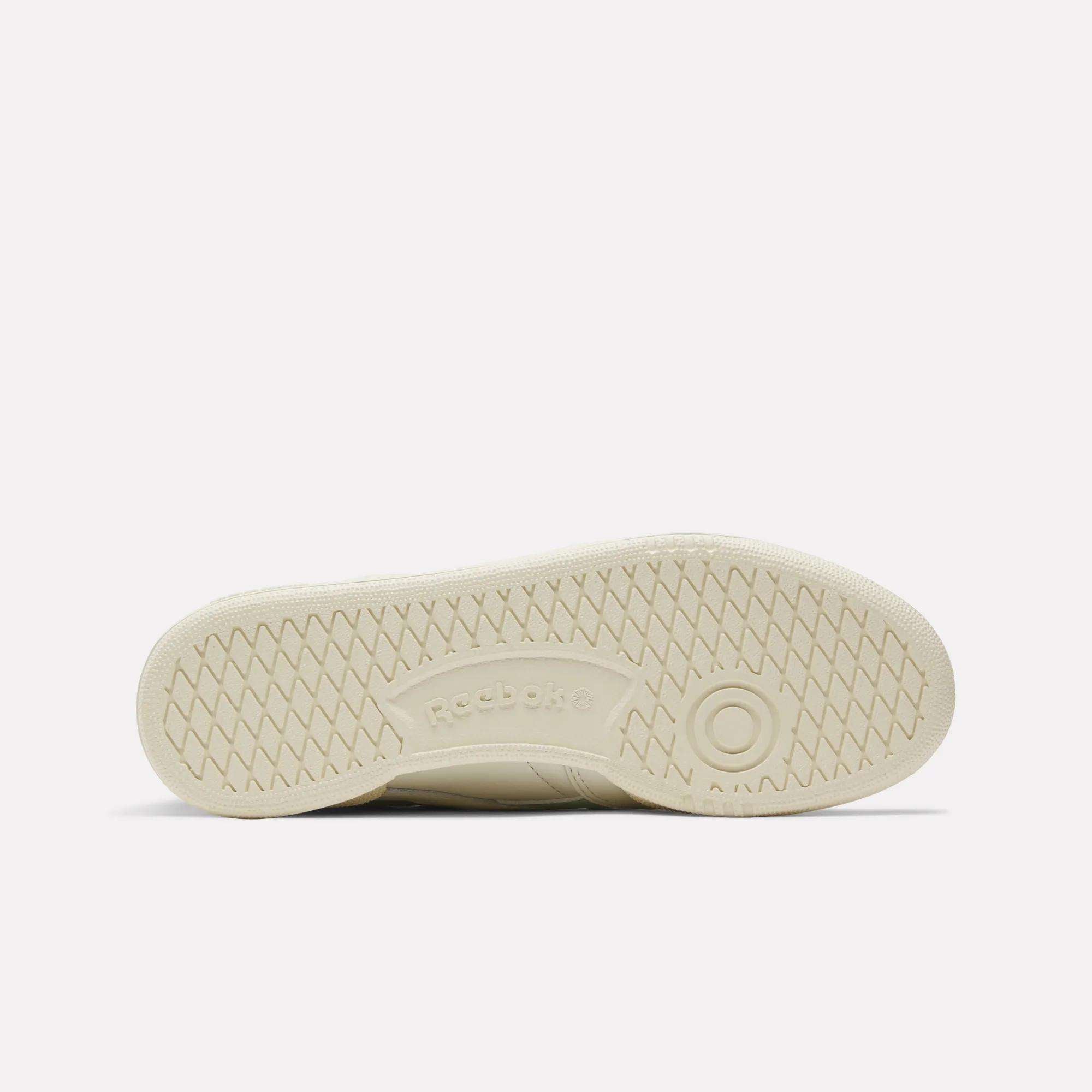 The image displays the off-white rubber sole of the Reebok Women's Club C Revenge Vintage Shoes, seen from below. It features a herringbone tread, a circular toe detail, and an embossed Reebok logo in the center—a classic retro look.