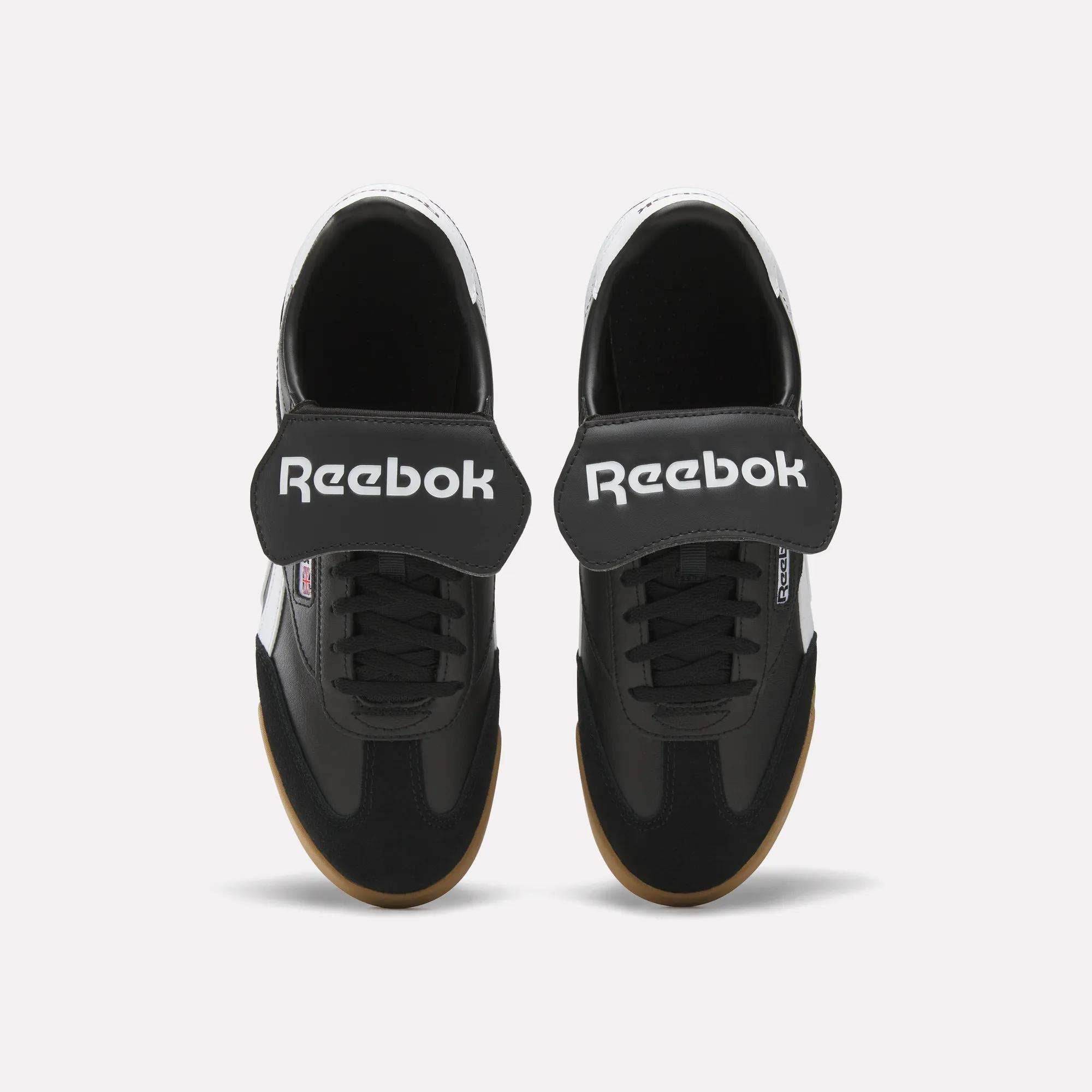Top view of Reebok Campio XT Kilty Shoes in black with wide Velcro straps, white Reebok logo, black laces, and light brown soles. These tennis-inspired sneakers are shown on a plain white background.