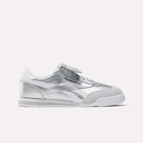 A pair of Reebok Campio XT Kilty Shoes featuring silver color, white and gray accents, tennis-inspired low-top design, and the Reebok logo on the side, showcased against a plain white background.