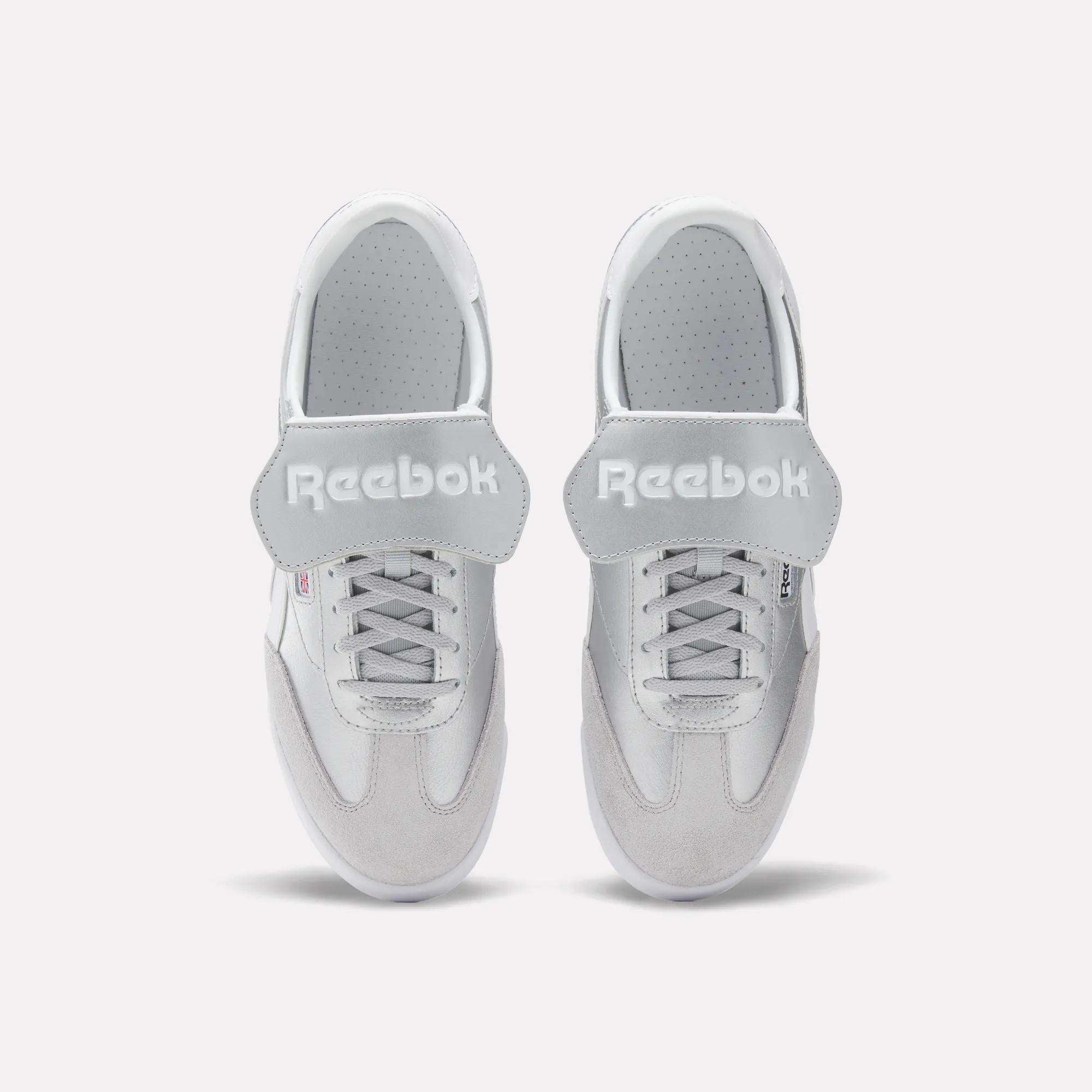 A pair of Reebok Campio XT Kilty Shoes in white leather are shown from above, side by side on a plain white background. They feature laces, wide velcro straps across the top, and the Reebok logo in white text.