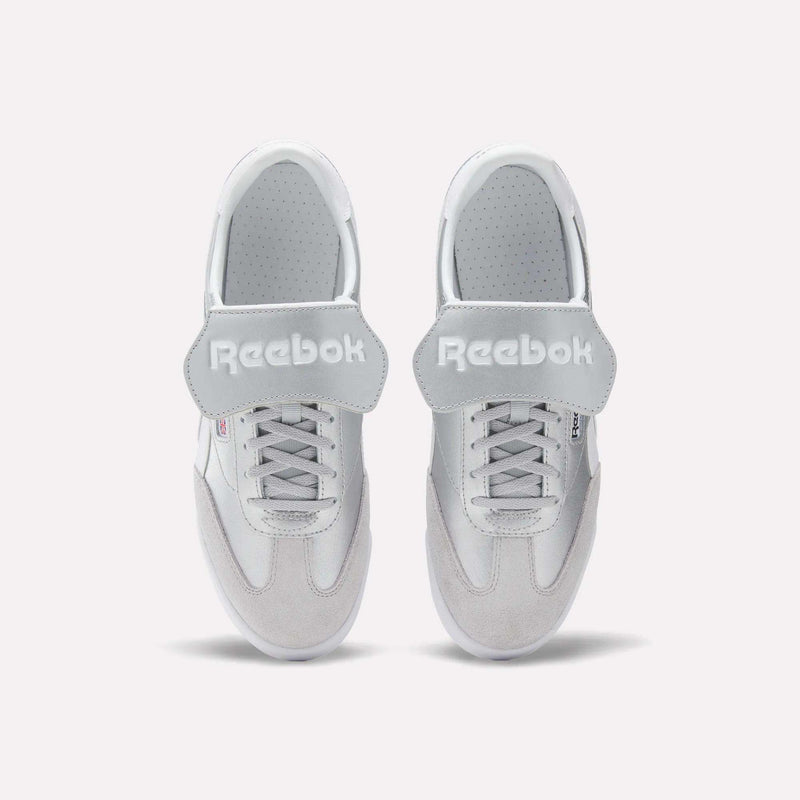 A pair of Reebok Campio XT Kilty Shoes in white leather are shown from above, side by side on a plain white background. They feature laces, wide velcro straps across the top, and the Reebok logo in white text.