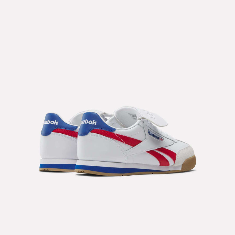 The Reebok Campio XT Kilty Shoes, made of white leather with blue heel tabs, red side stripes, and gum soles, are angled on a plain white background to highlight their tennis-inspired style.