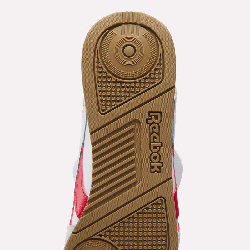 Close-up view of the sole of Reebok Campio XT Kilty Shoes, showing a textured gum rubber pattern and embossed Reebok logo. Red and white accents accentuate the tennis-inspired leather upper for a stylish finish.