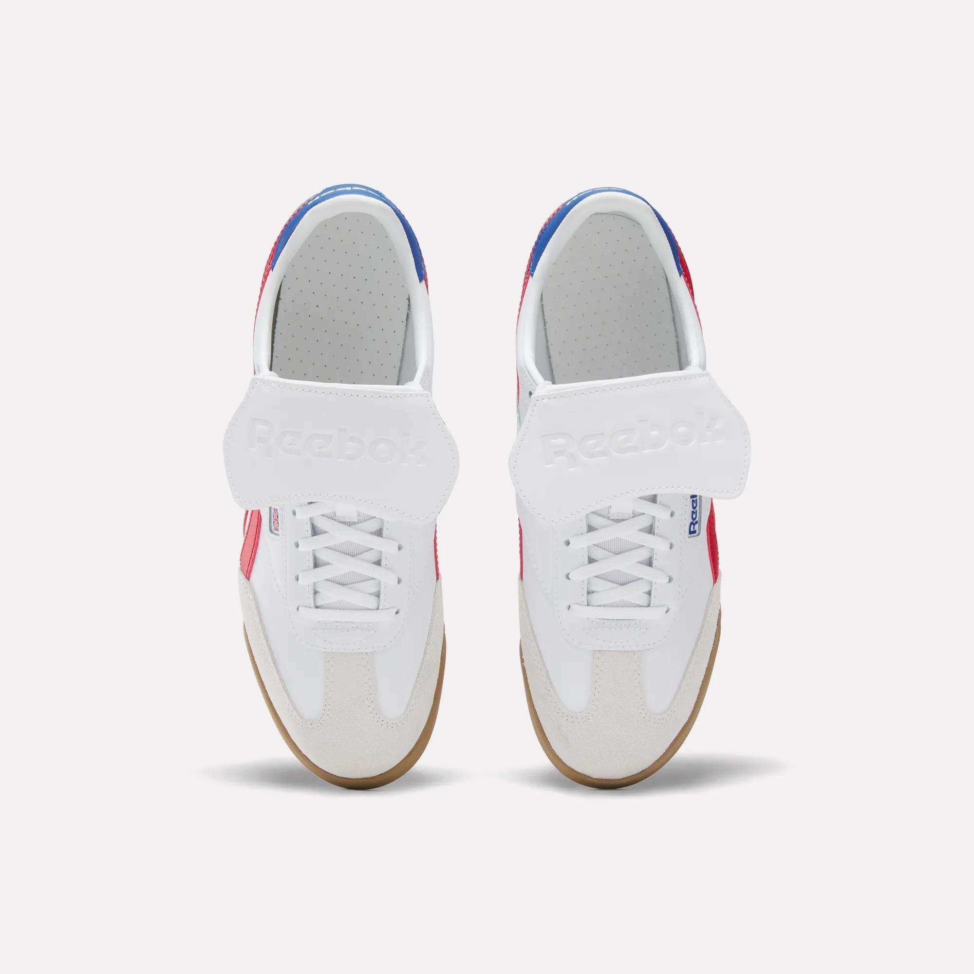 Top view of Reebok Campio XT Kilty Shoes: white tennis-inspired design with velcro straps, beige toe caps, gum soles, and red and blue accents on sides and heel, set against a plain light background.