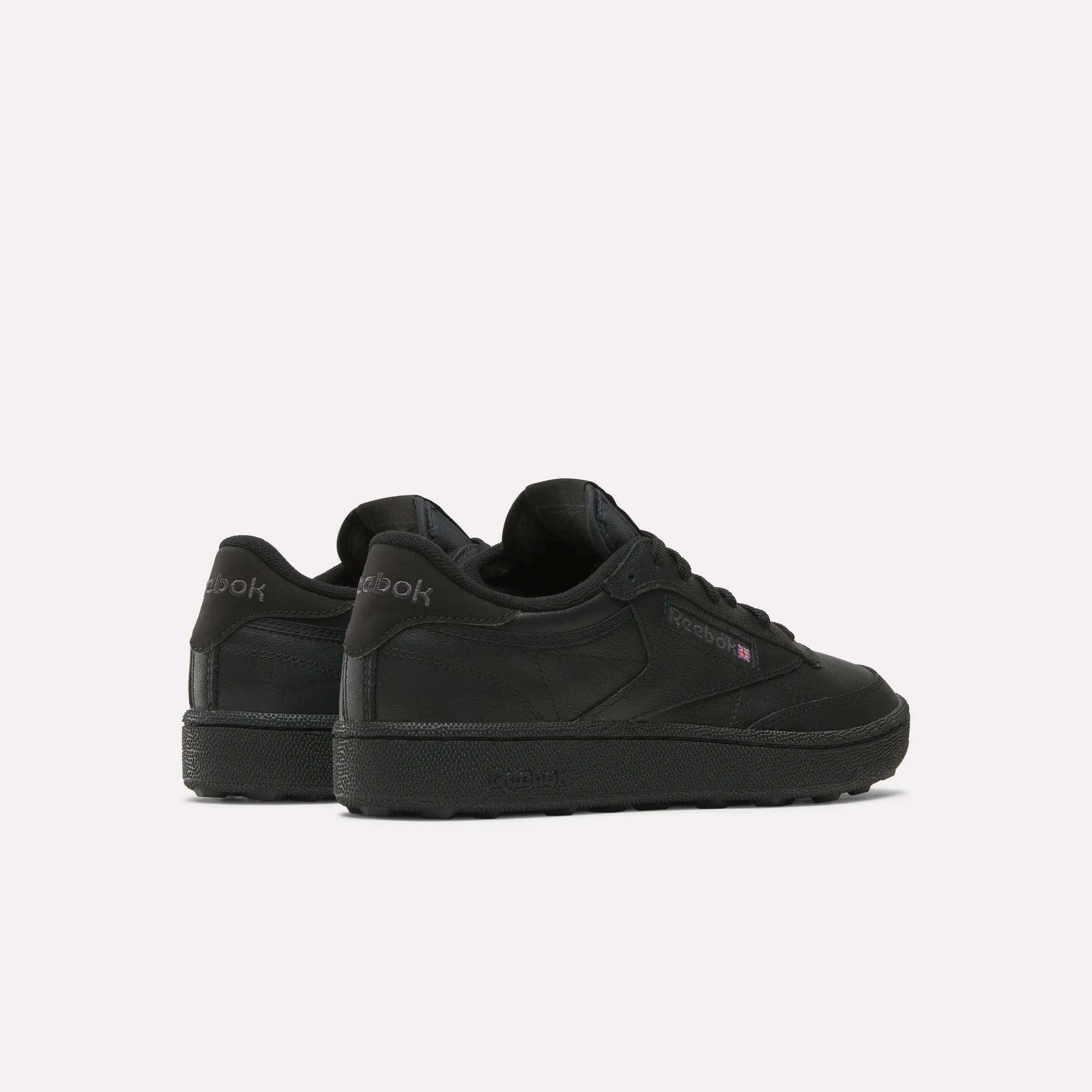The Reebok Men's Club C Golf Shoes in black feature a low-top, spikeless design. Displayed from the back and side on a white background, the Reebok logo appears on both the heel and side.