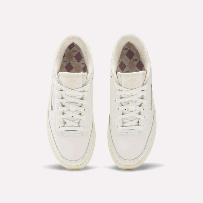The Reebok Women's Club C Golf Shoes are white, spikeless, lace-up golf shoes with a water-resistant leather upper, minimalist design, and a subtle checkered inner lining.