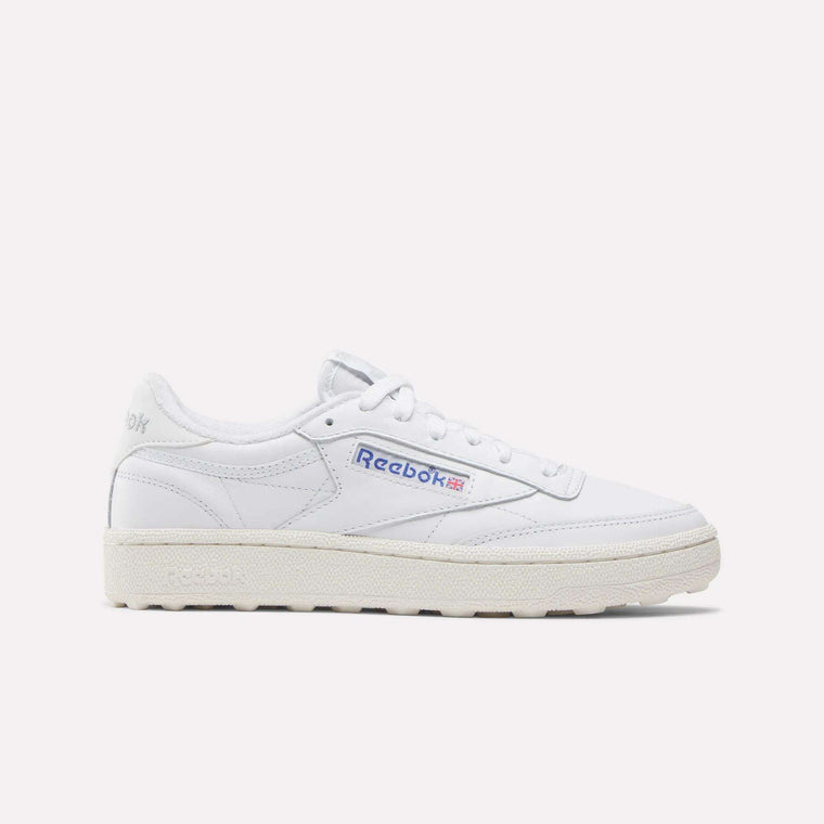 The Reebok Women’s Club C Golf Shoes feature a white upper, cream sole, blue and red side logo, spikeless outsole, and white laces, shown against a plain white background.