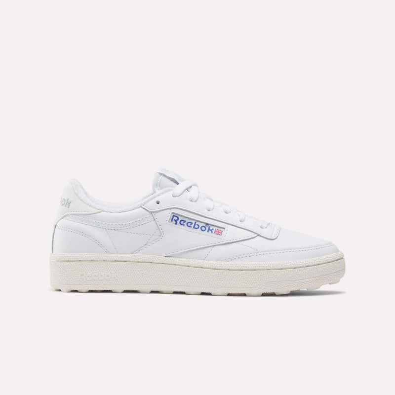 The Reebok Women’s Club C Golf Shoes feature a white upper, cream sole, blue and red side logo, spikeless outsole, and white laces, shown against a plain white background.