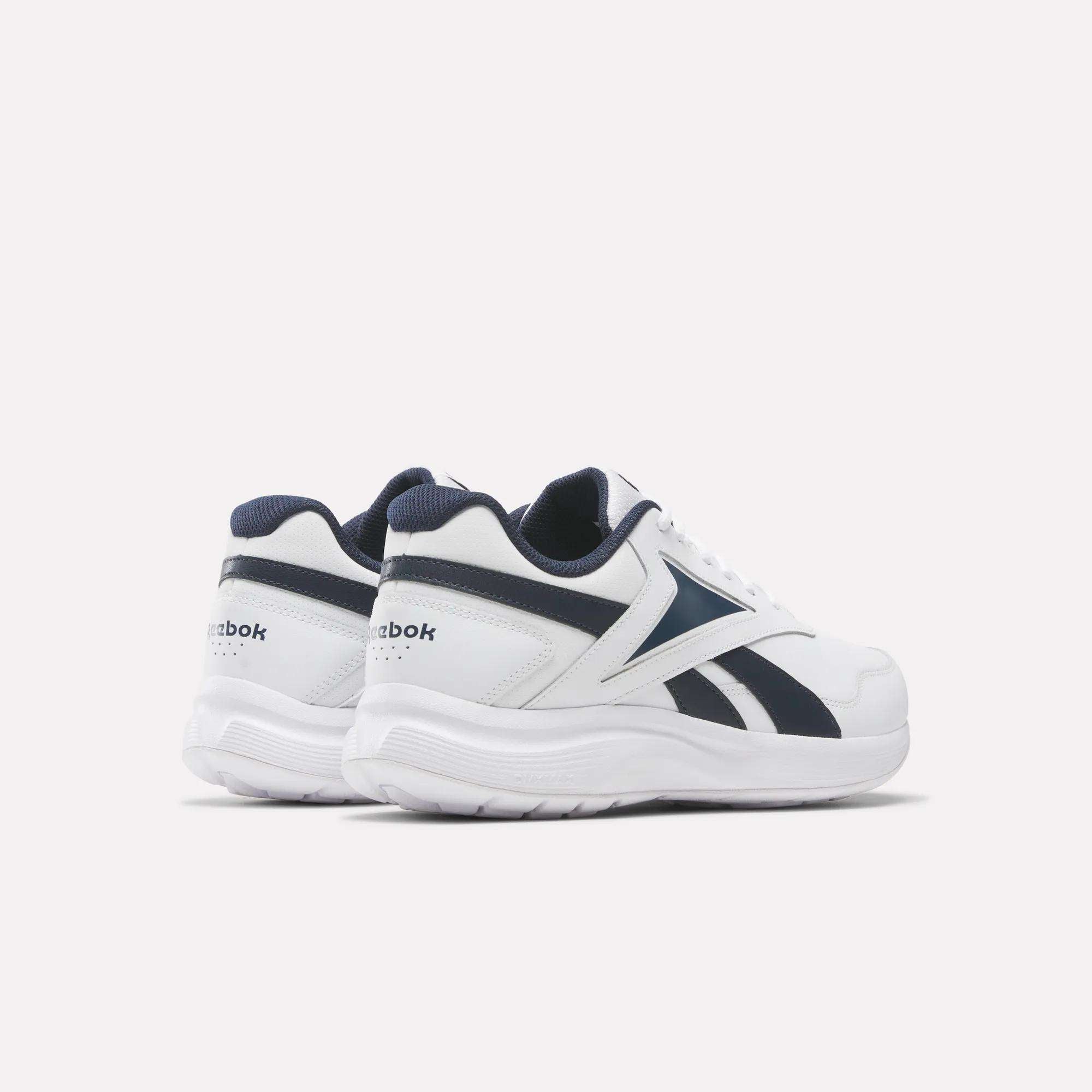 A pair of Reebok Men's Walk Ultra 7 DMX Max Wide 4E Shoes in white with navy accents, displaying the Reebok logo and a chunky, air-cushioned sole, shown at an angle on a plain light background.