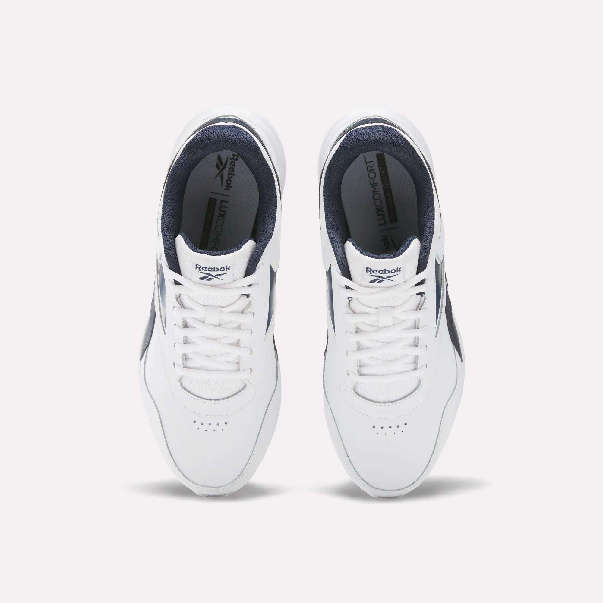 Top view of Reebok Men's Walk Ultra 7 DMX Max Wide 4E Shoes in white with navy accents and white laces, side by side on a light background. These wide-fit walking shoes offer comfort and style, featuring insoles with the Reebok logo.