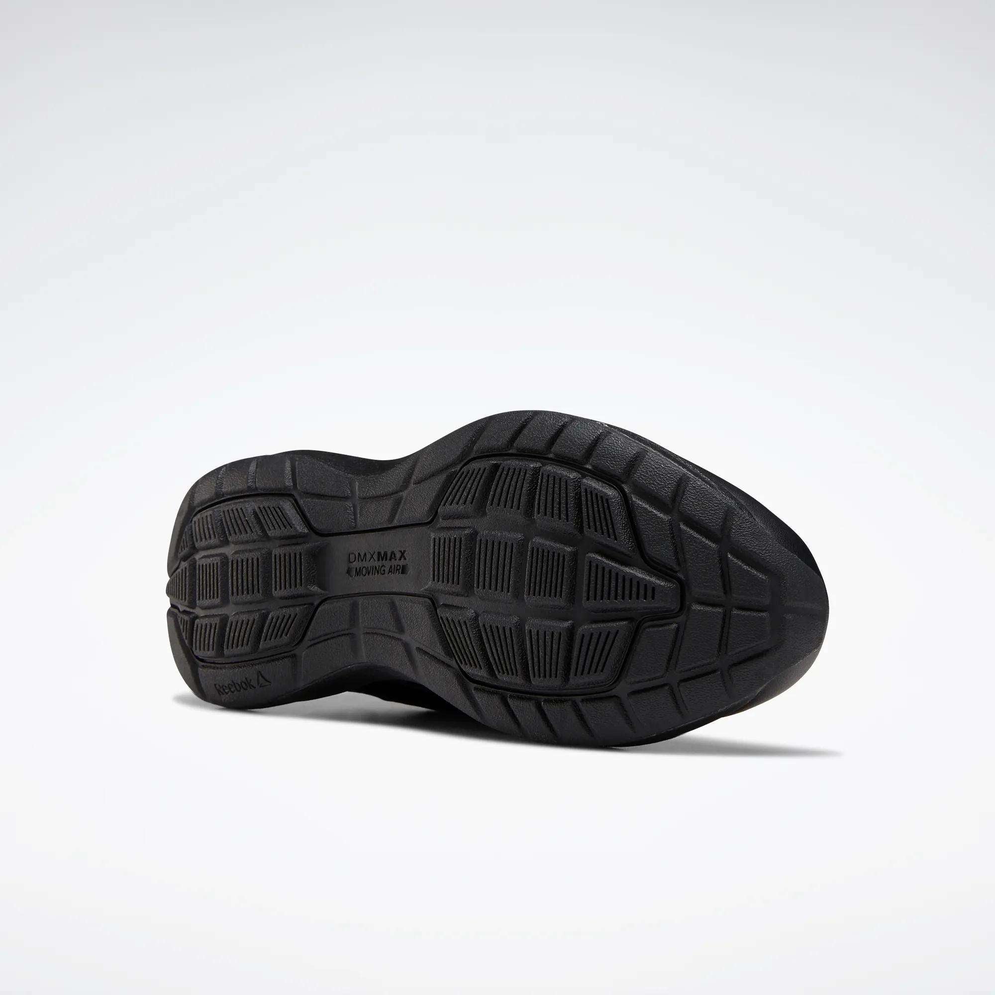 The image shows the black rubber outsole of the Reebok Women's Walk Ultra 7 DMX Max Walking Shoes, featuring a textured tread pattern and "DMX MAX MOVING AIR" text highlighting its advanced cushioning, viewed from the bottom on a light gray background.