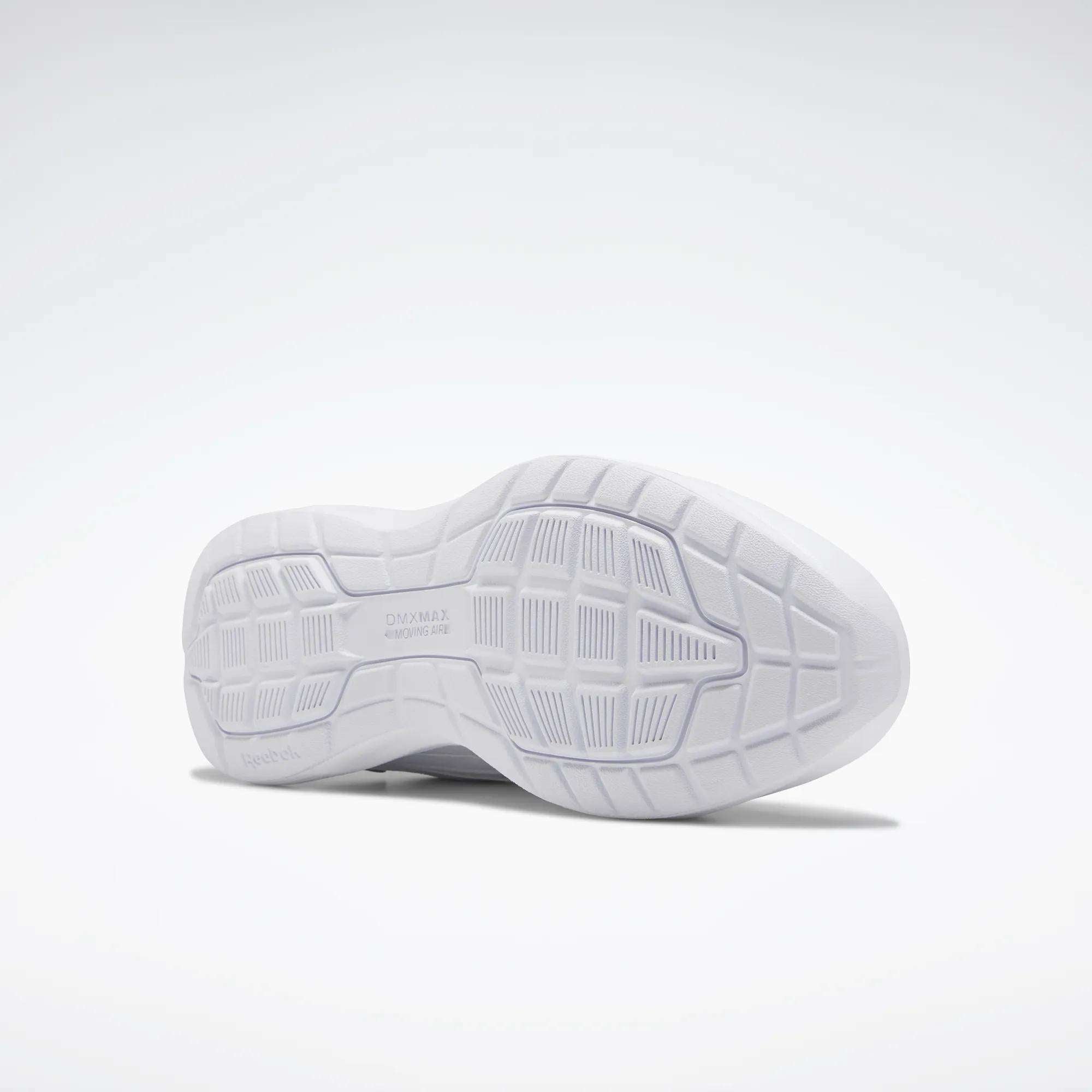 The image shows the sole of a Reebok Women's Walk Ultra 7 DMX Max Walking Shoe. Its white, textured grip and DMX cushioning enhance comfort. The shoe is positioned on its side against a plain, light background.