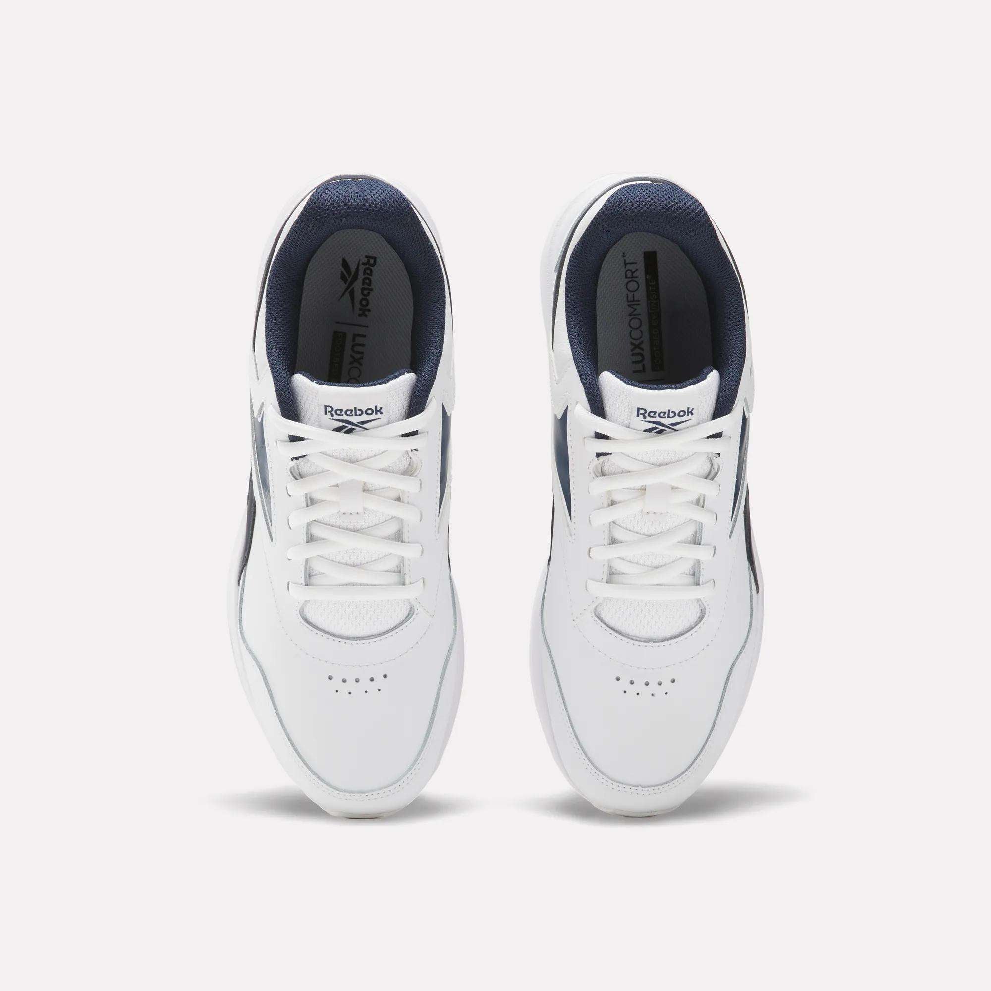 Top view of a pair of Reebok Walk Ultra 7 DMX Max walking shoes in white with navy blue accents, breathable mesh uppers, white laces, and the Reebok logo on the tongue and insole, placed side by side on a light background.