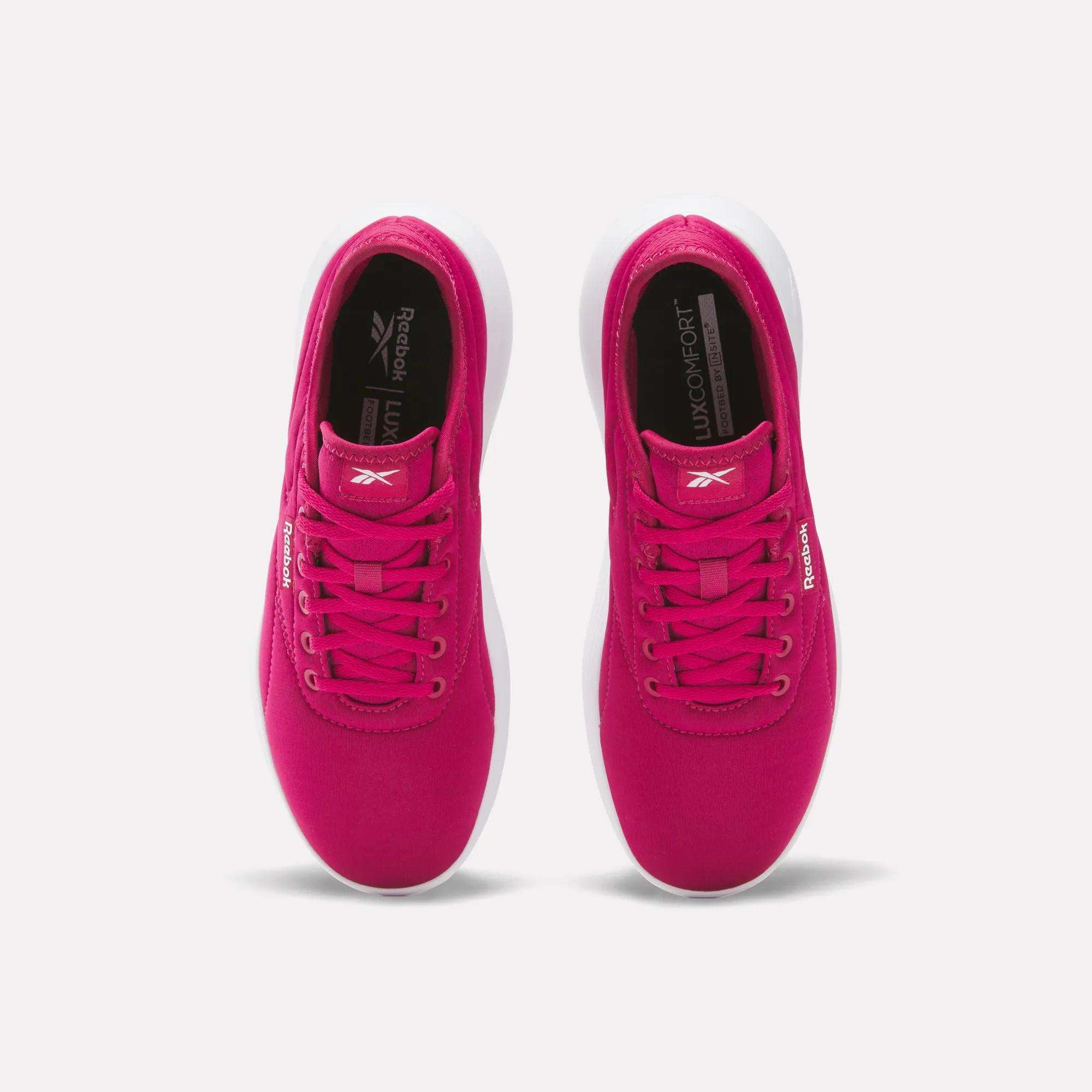 A pair of Women's Active Lite Shoes by Reebok in bright pink, seen from above with white soles, pink laces, and “Reebok” logos on the tongue and side. These minimalist sneakers are side by side on a plain white background.