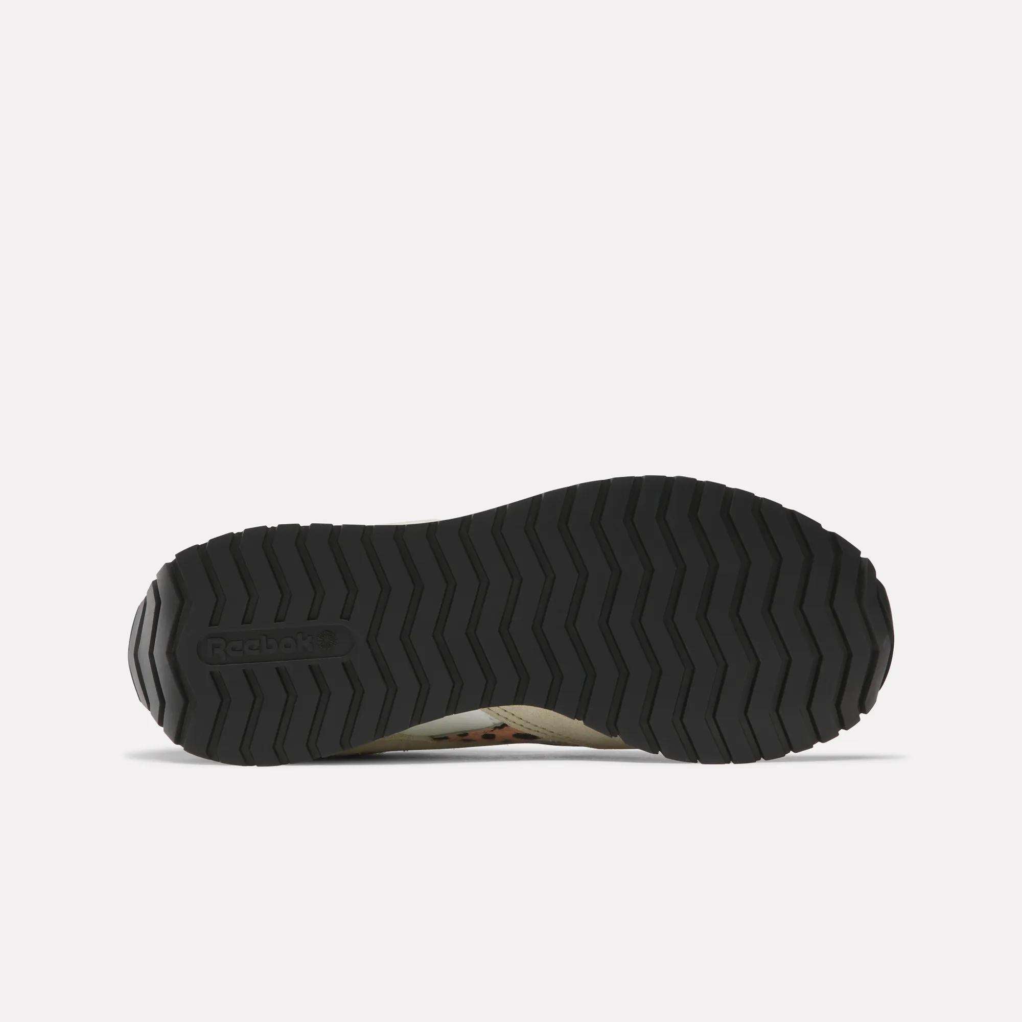 The image displays the black, textured rubber outsole of Reebok Women's Classic AZ Shoes from the bottom on a plain white background, showing a zigzag tread pattern with the Reebok logo on the left side.