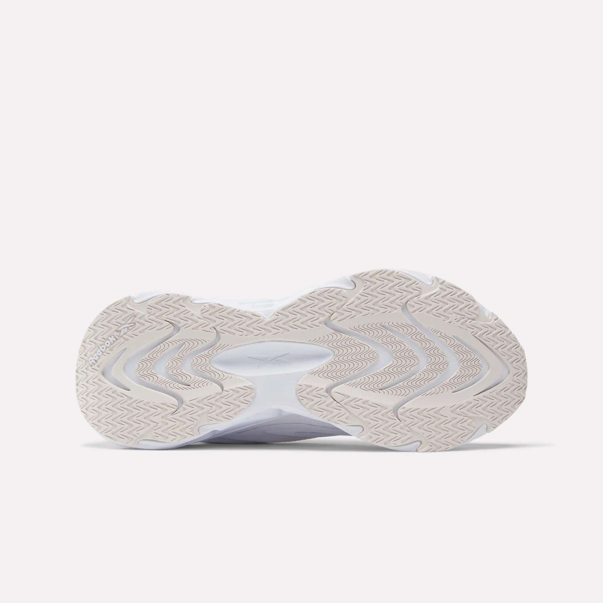 The image shows the sole of a white Reebok Women's Fuel Flex Run Shoe with a beige, wavy tread and zigzag details, viewed from below against a light background, emphasizing the cushioning Fuel Flex midsole.