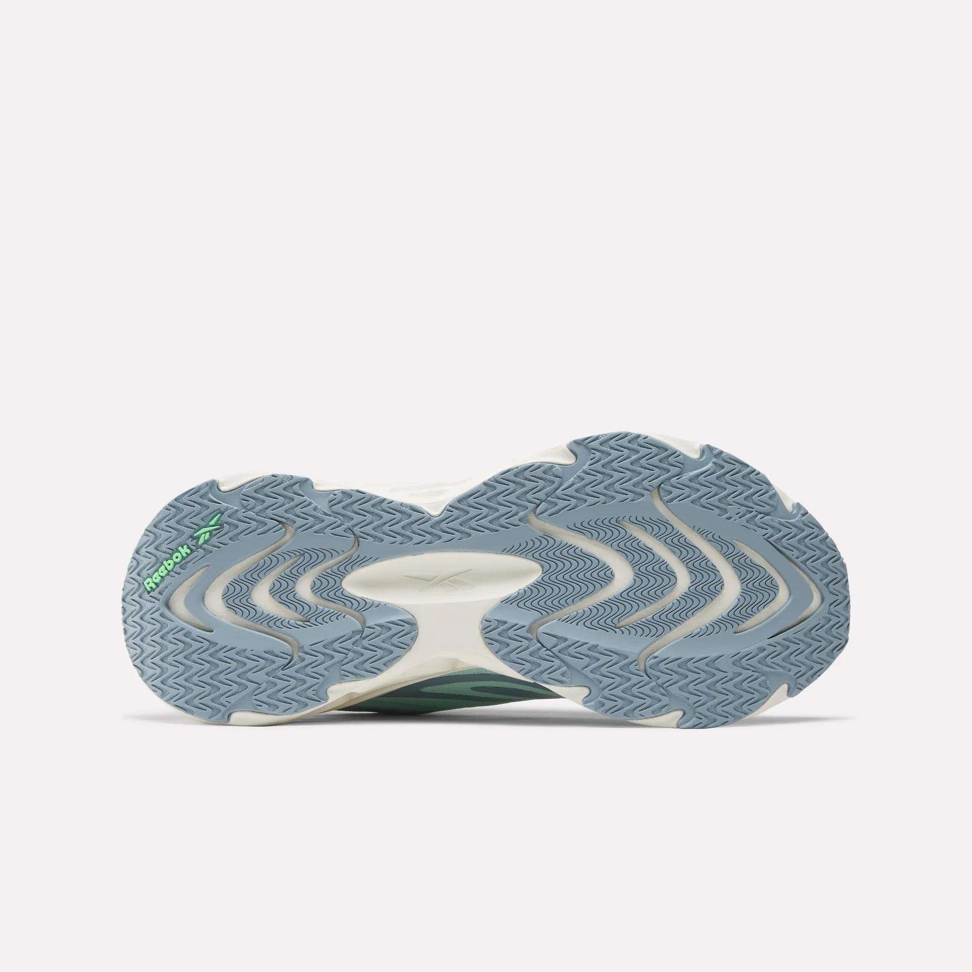 The image displays the sole of Reebok Women's Fuel Flex Run Shoes, showcasing a wavy blue and gray tread with white and green accents. The textured outsole and Fuel Flex midsole provide excellent traction and lasting comfort.