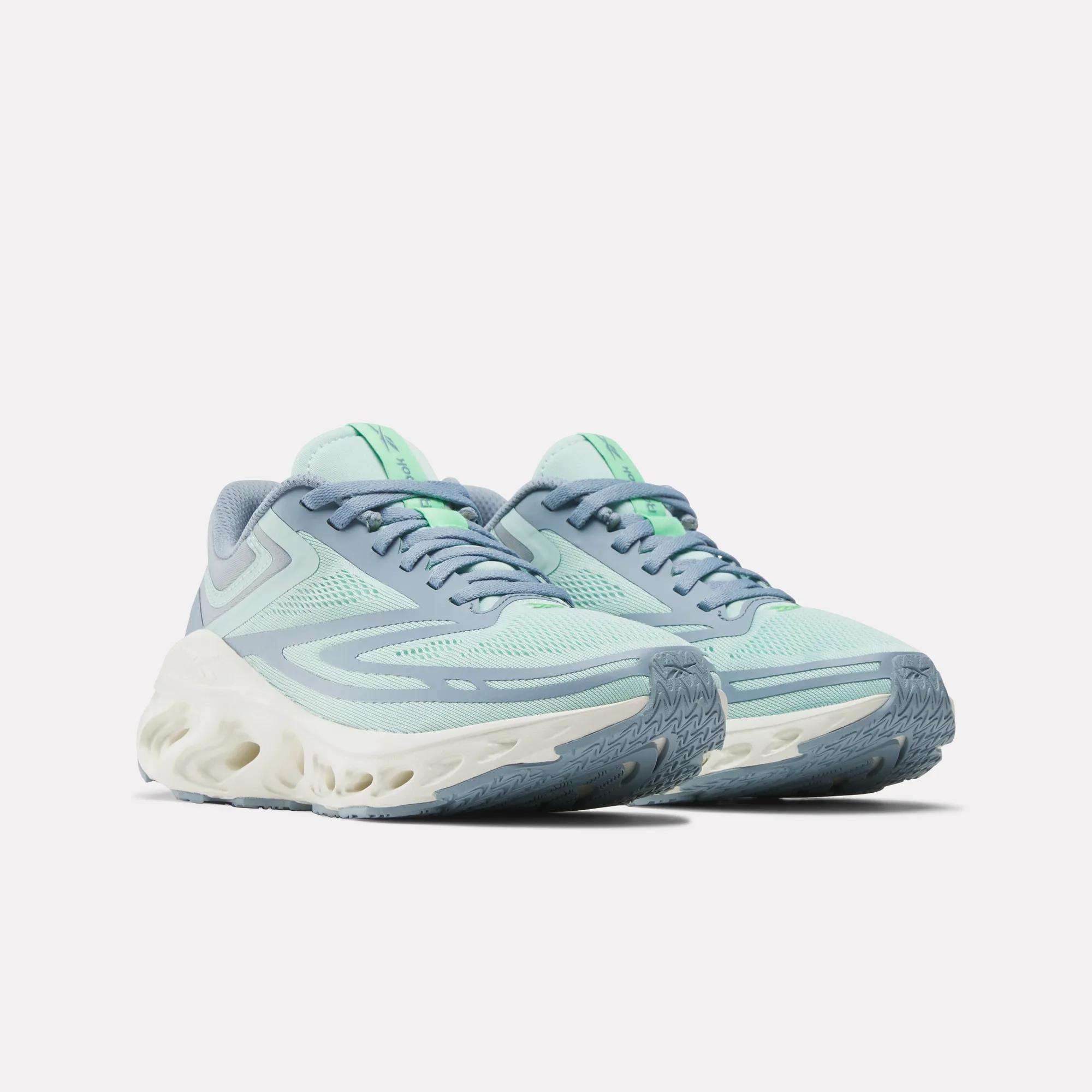 The Reebok Women's Fuel Flex Run Shoes, shown in light blue and mint green with white sculpted soles and patterned tread, offer long-lasting comfort with a Fuel Flex midsole. They are displayed against a plain white background.