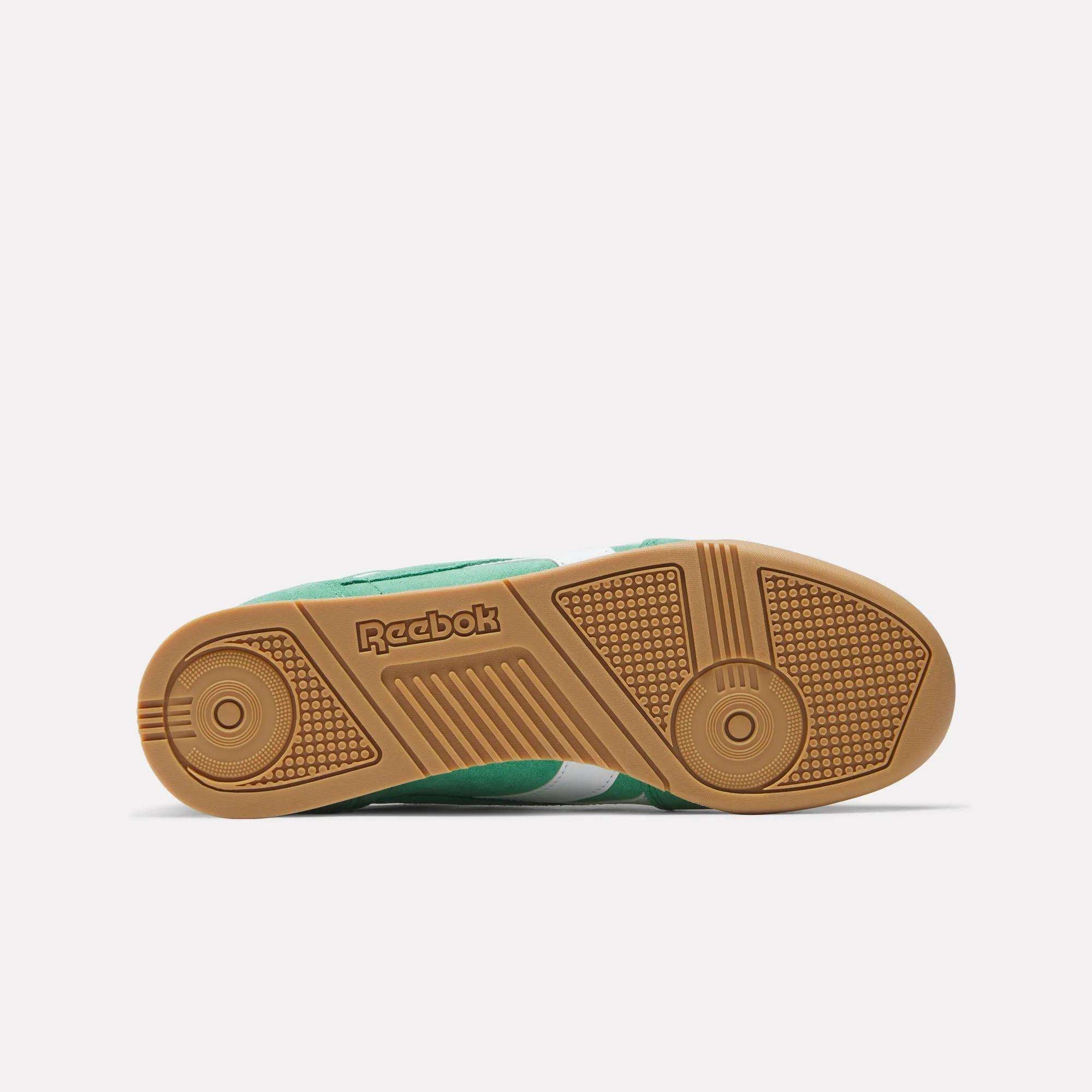 The image displays the sole of a green Reebok Campio XT Shoe, highlighting its '90s soccer-inspired design with a gum rubber outsole, circular textured grip patterns, and an embossed Reebok logo in the center.