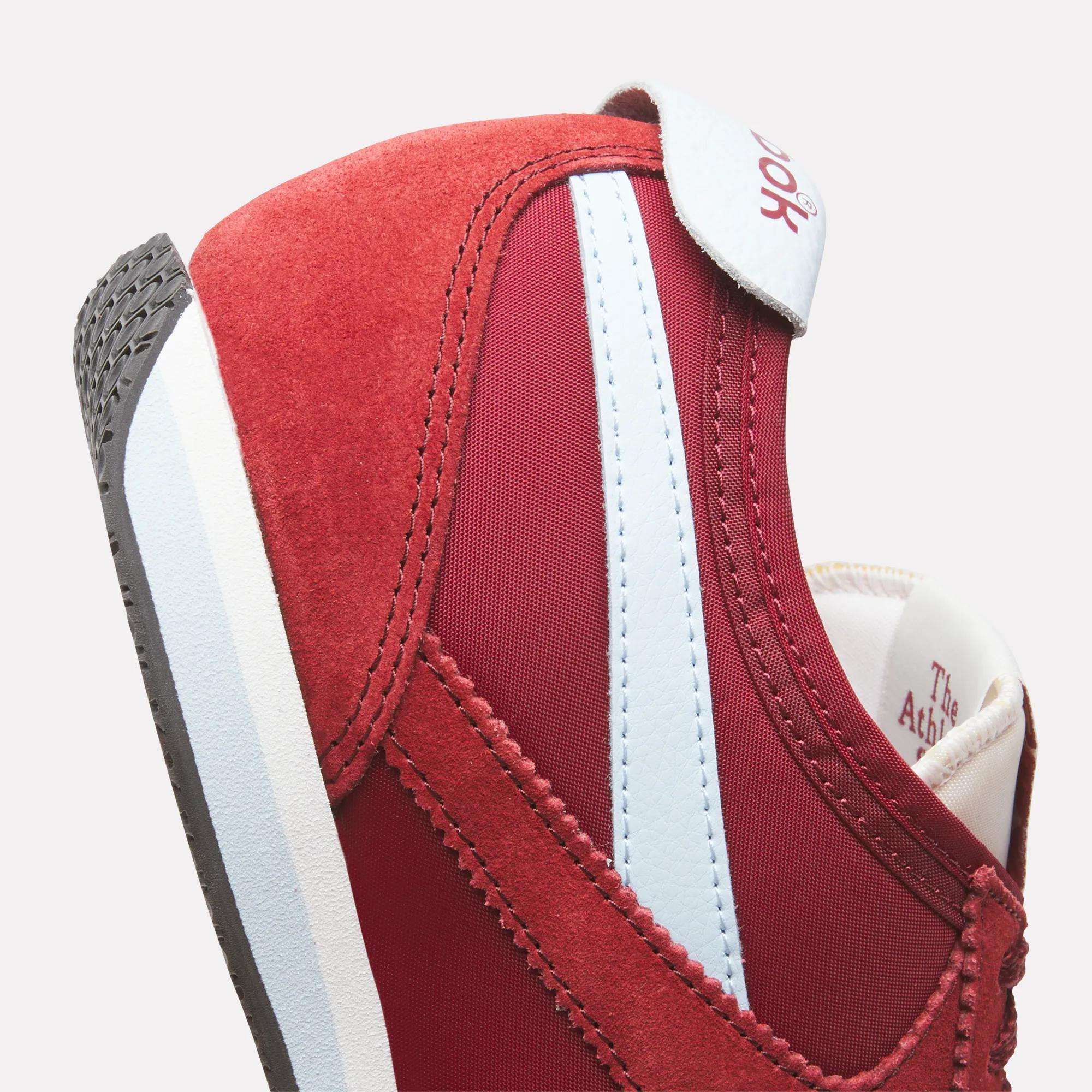 Close-up of red Reebok R400 Shoes with light blue and white stripes, suede and mesh details, visible side stitching, plus parts of the tongue and heel for a classic low-profile look.