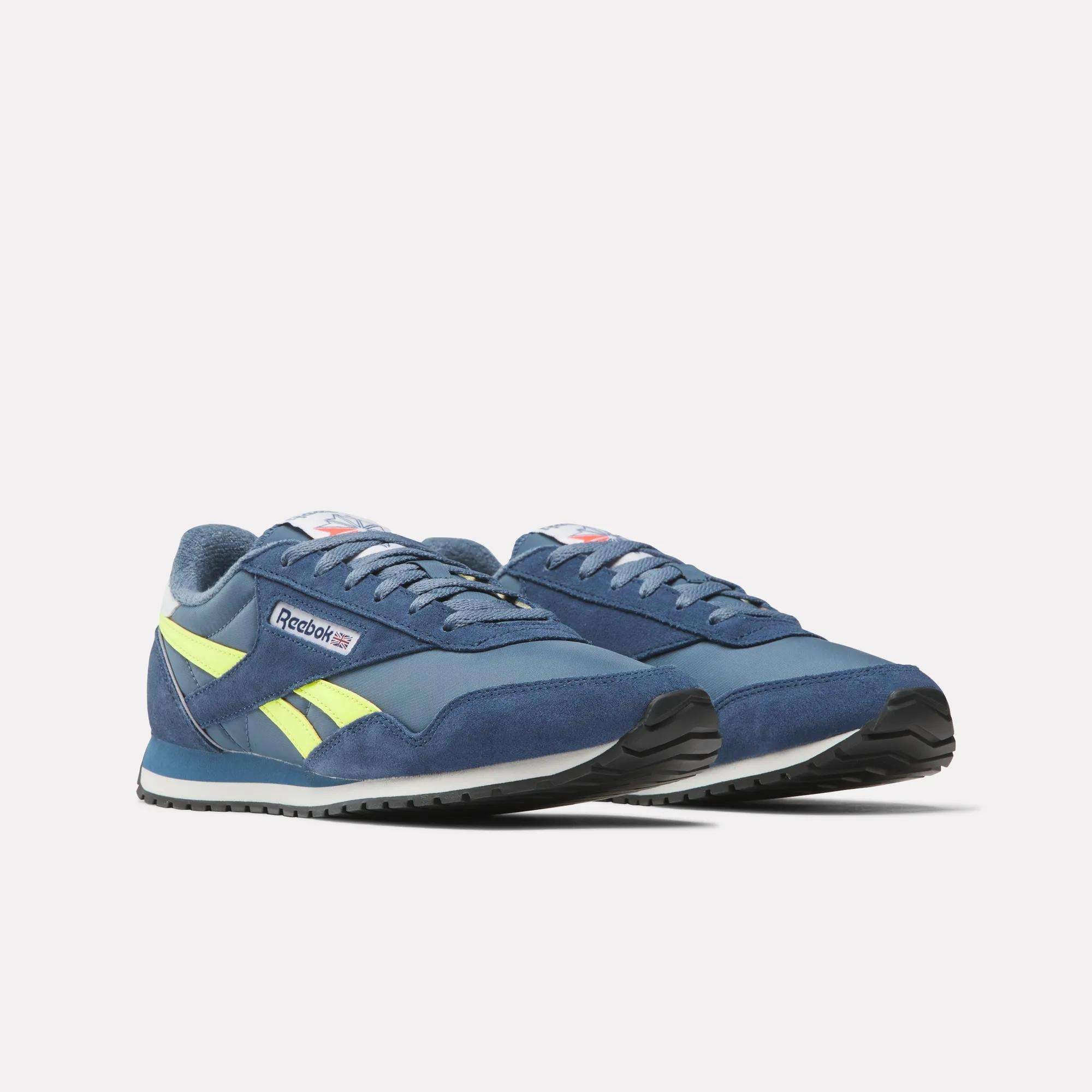 A pair of Classic AZ Shoes by Reebok in blue with yellow accents and white soles, displayed on a plain white background. Shown at an angle to highlight their ‘70s-inspired retro running style.