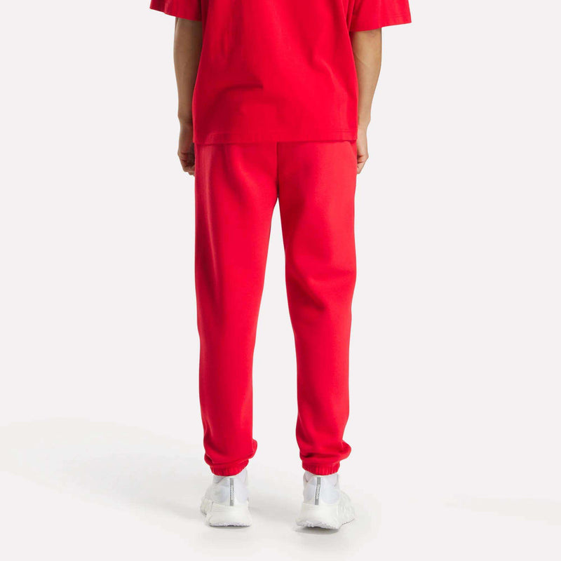 A person stands with their back to the camera, wearing a red T-shirt, Reebok Men's Joggers, and white sneakers against a plain white background.