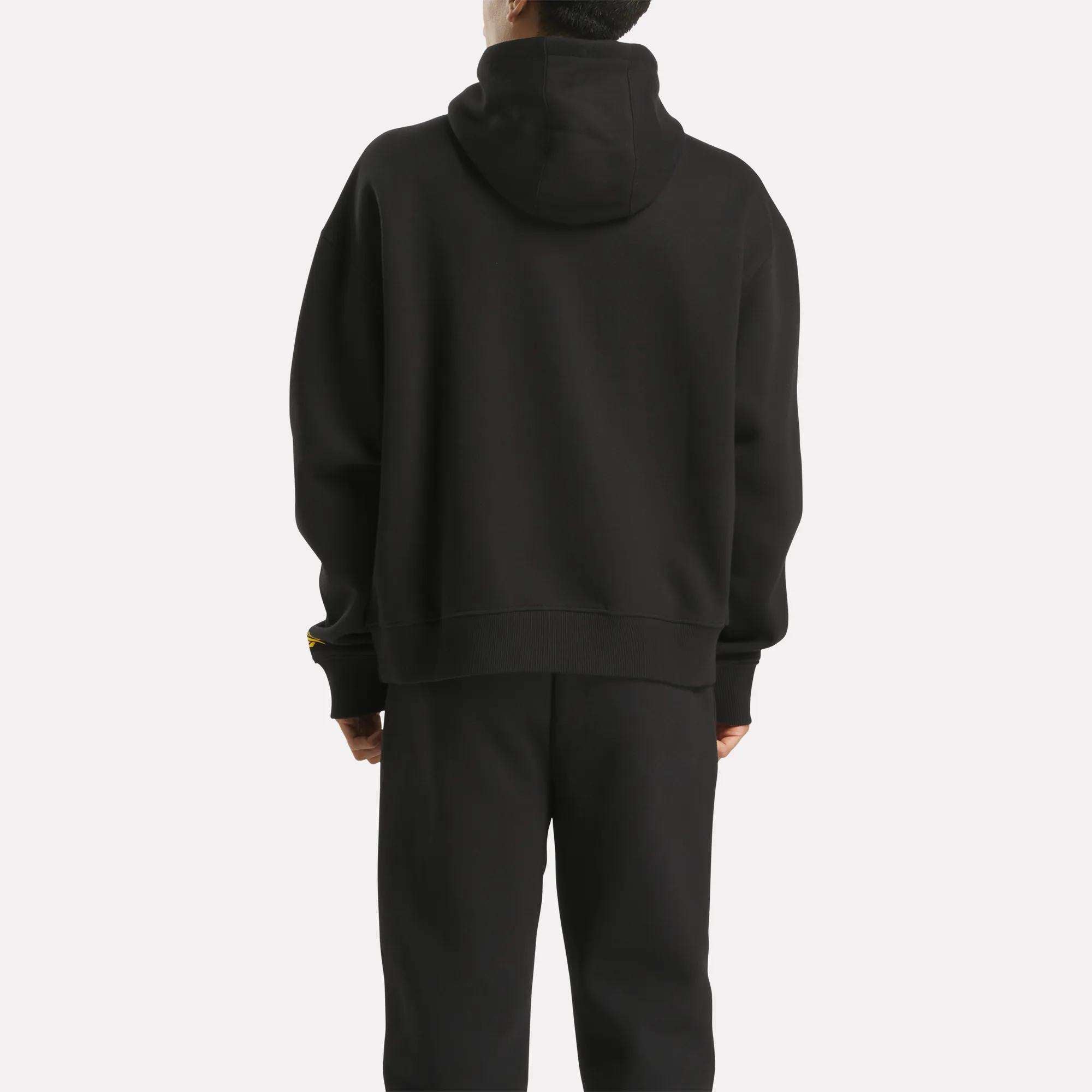 A person stands with their back to the camera, wearing a Men's Hoodie by Reebok in black, paired with matching black pants against a plain white background.