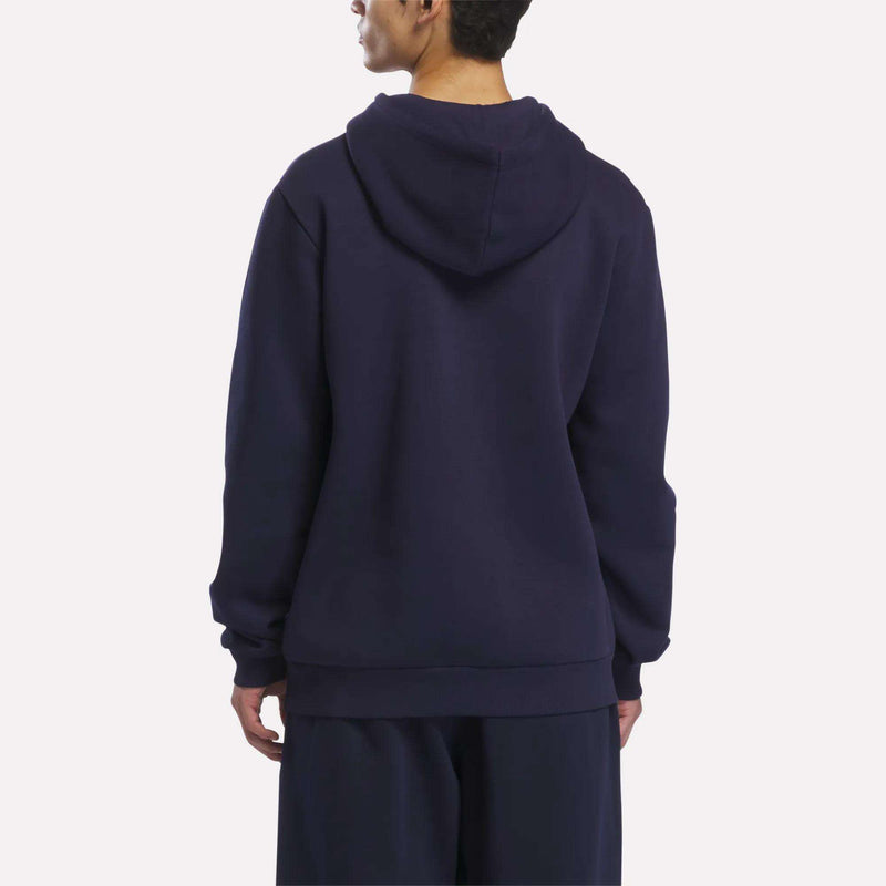 A person is standing with their back to the camera, wearing a Reebok Men’s Logo Hoodie in dark blue and matching pants against a plain, light background.